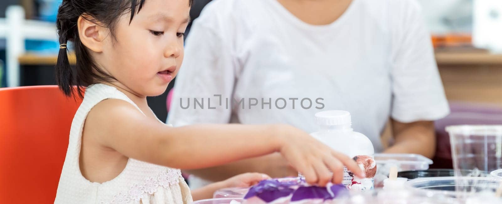 Panoramic asian girl kid playing colorful paper for art lesson at living room in home as home schooling while city lockdown because of covid-19 pandemic across the world with quaratine mom as teacher.