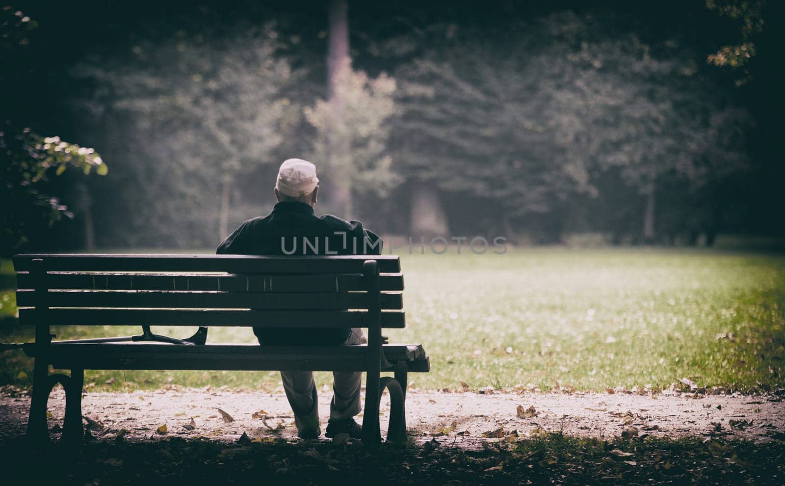 a lonely old man sitting on a bench in a park