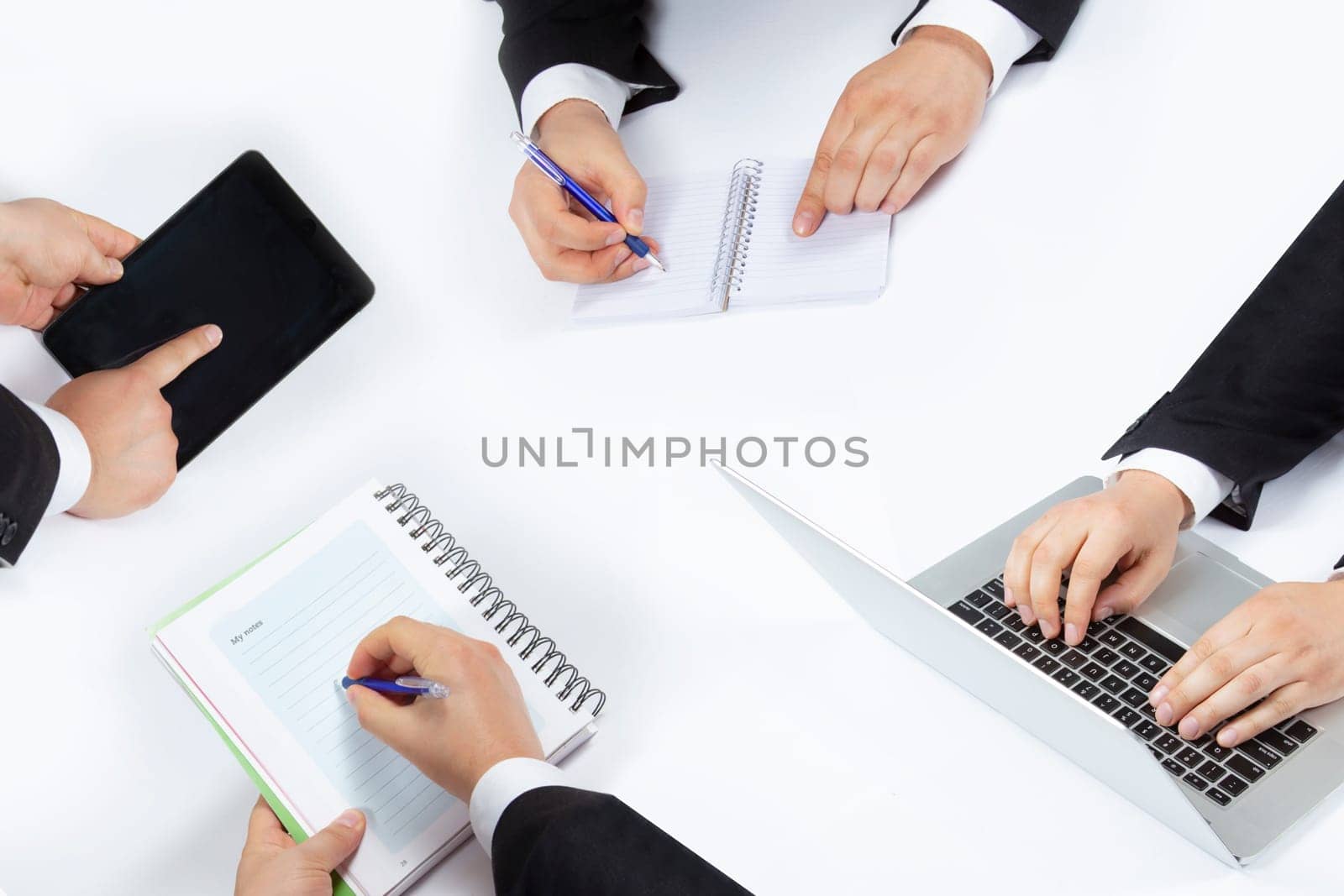 Hands of business people during a meeting working. Taking notes, using a tablet and a laptop.