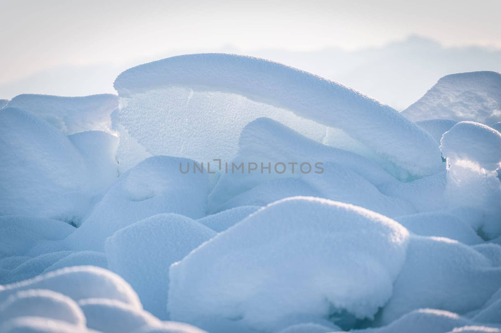 Transparent blue ice floes piled in ice hummocks against a blue sky on a sunny day. Unusual winter landscape of the frozen lake Baikal. Natural cold background. Siberia, Russia.