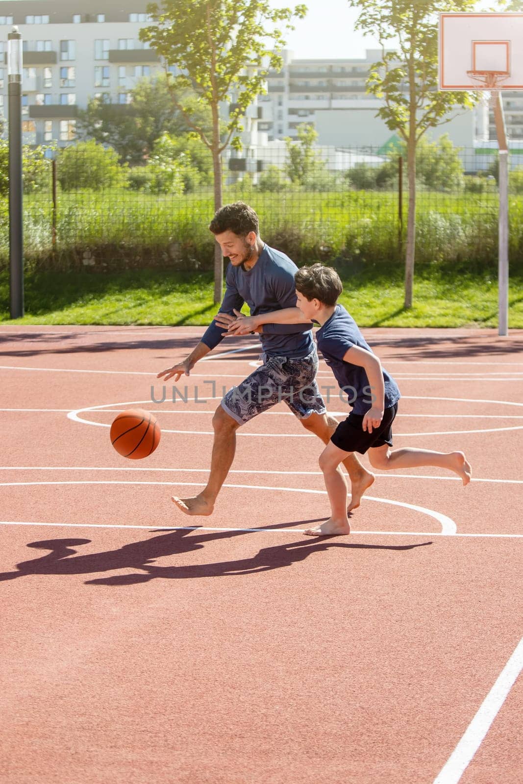 Father and son playing basketball barefoot with the ball on a playground