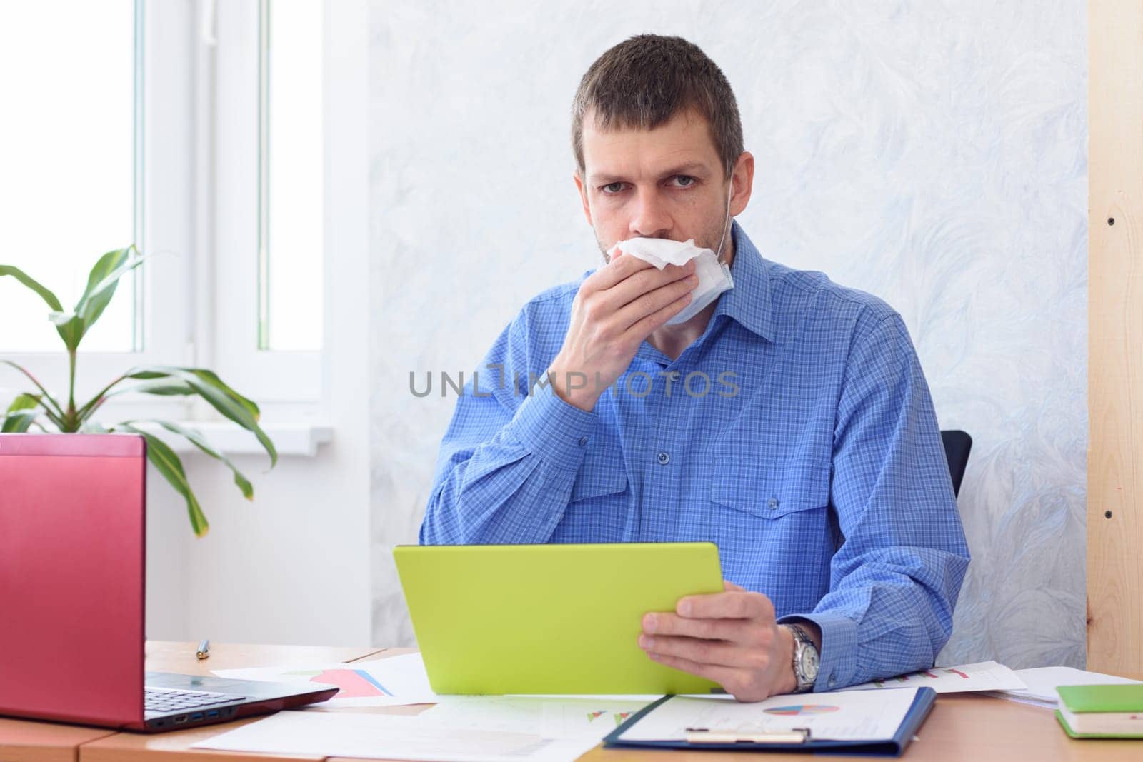 An office worker with a tablet in his hand holds a napkin at his mouth