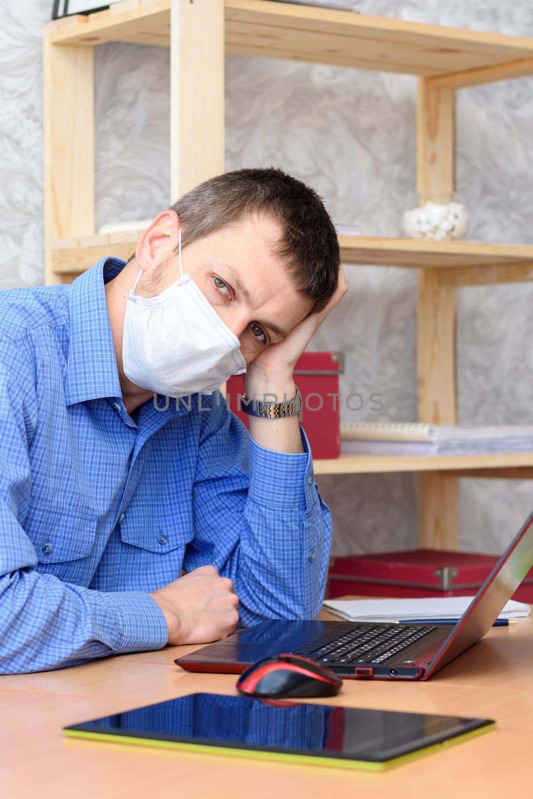 Sad leader sits behind a worker in front of a laptop wearing a protective mask