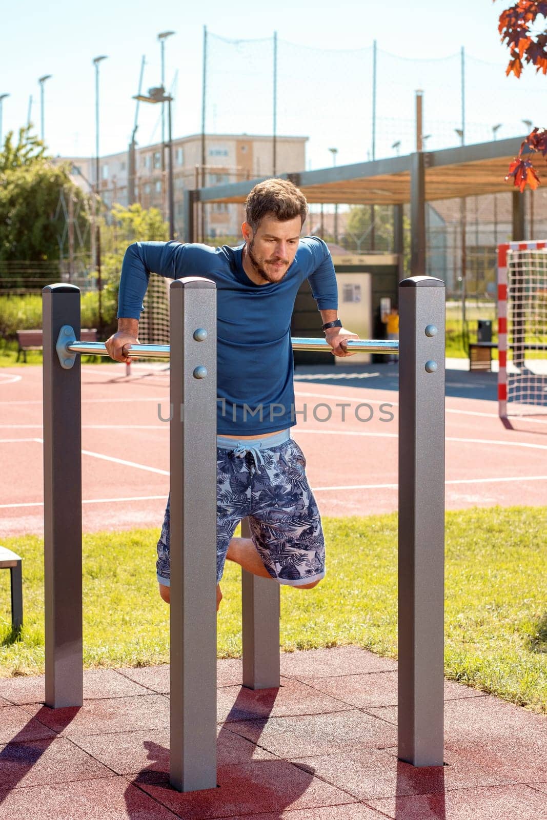 Young handsome man training at parallel bars in the playground on a sunny day
