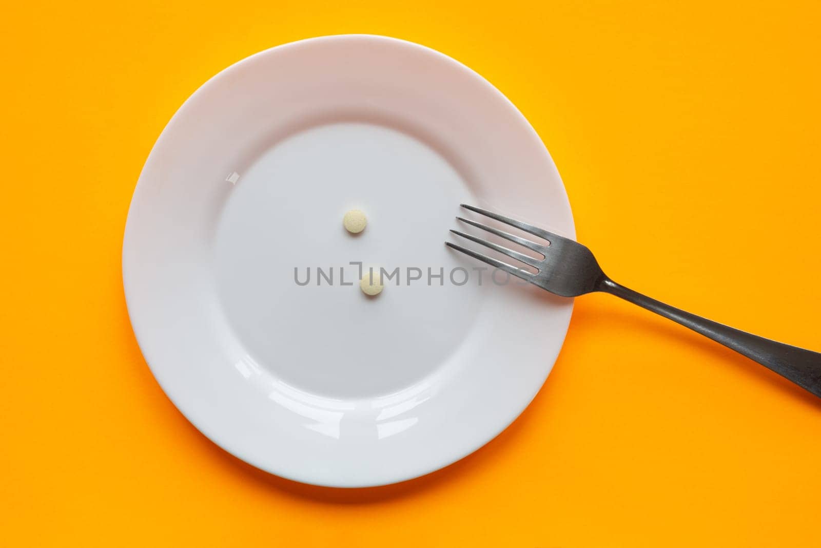 On the plate are two tablets and a fork, orange background