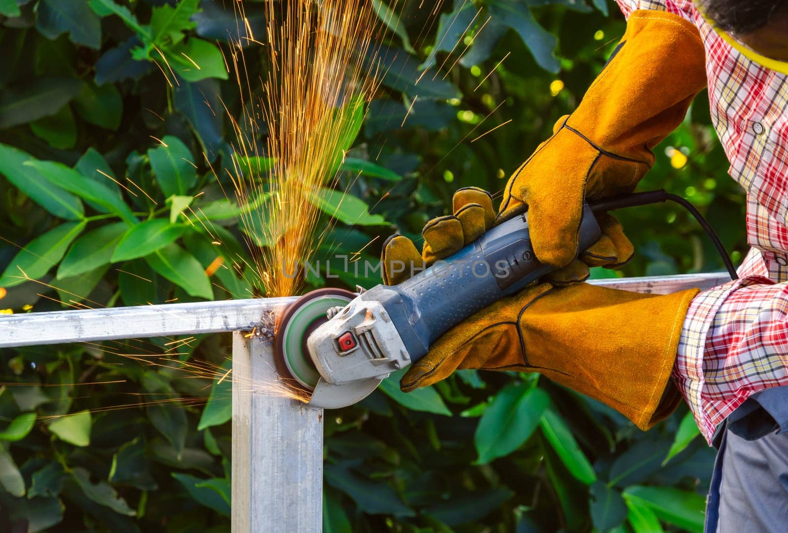 Worker wearing safety leather gloves with goggles and grinding arc welding strikes of structural steel frame with electric angle grinder. Industrial concept.