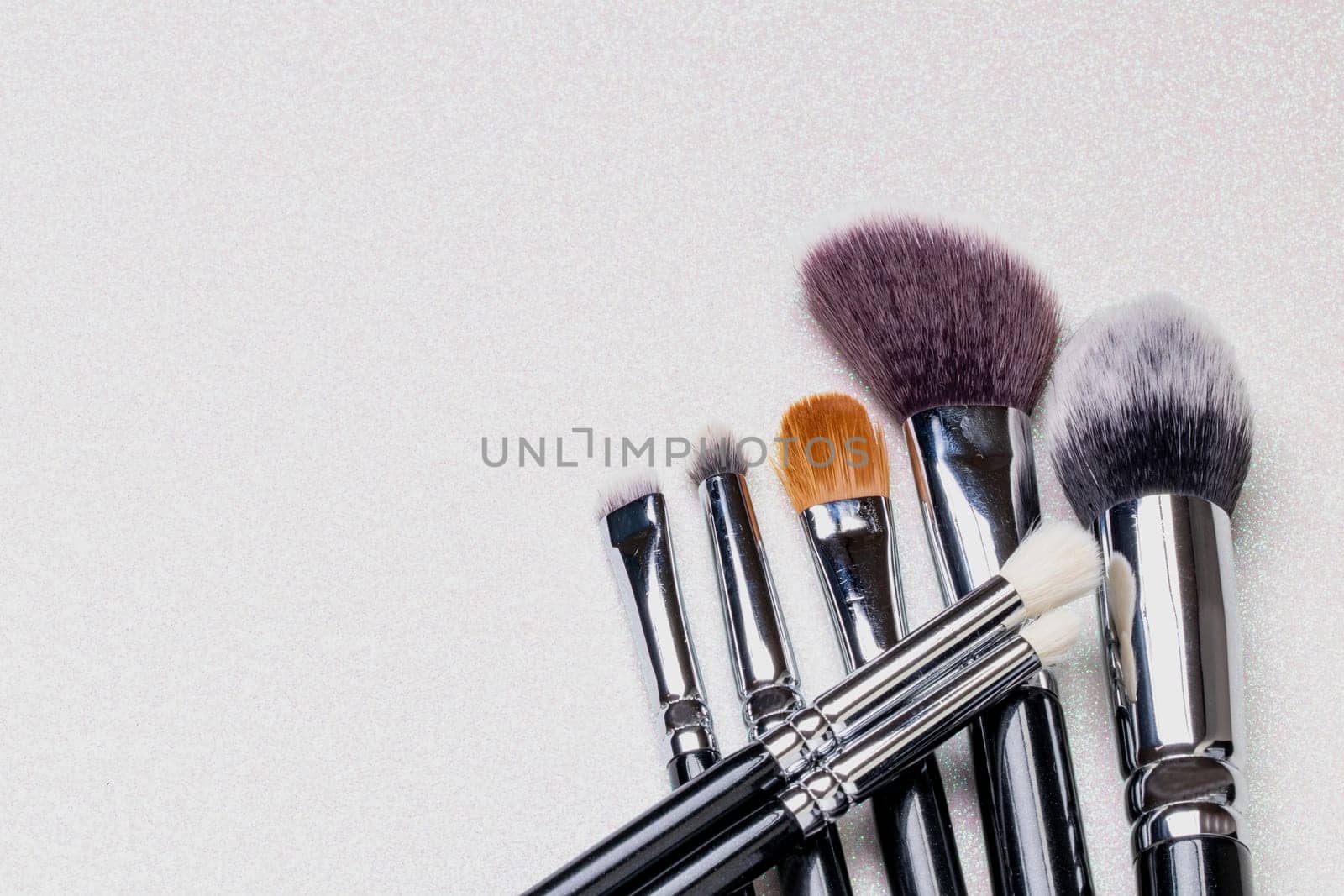 Closeup of a set of seven professional make up brushes on a bright glitter sparkle background with copy space. Template for cosmetics product display montage or advertising text. Macro.