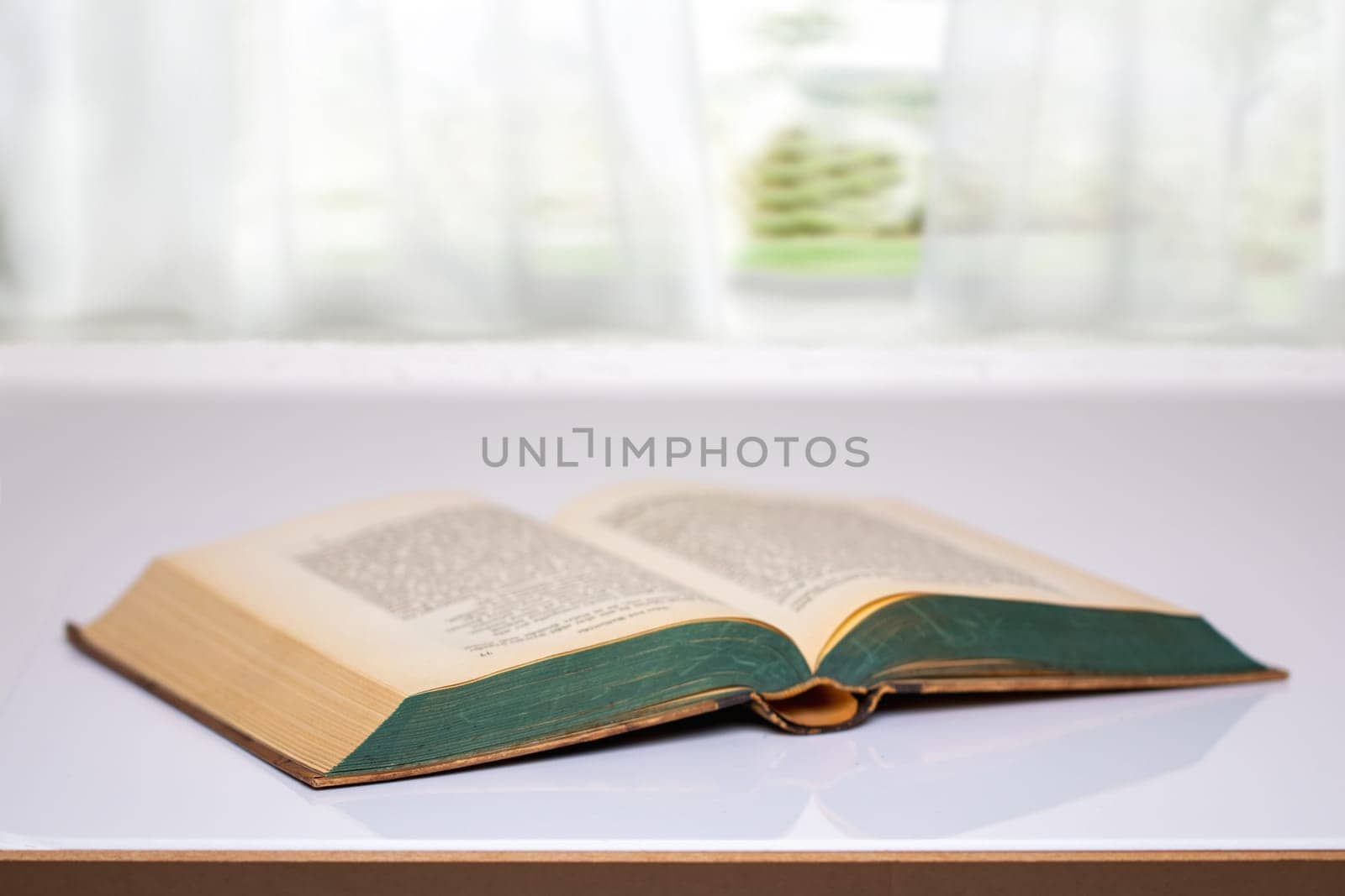Close-up of an opened antique book on a bright table with blurred natural background. Education concept.