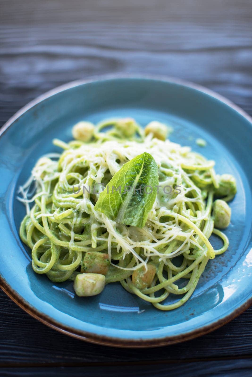 Green Pasta with scallop and sauce on blue plate