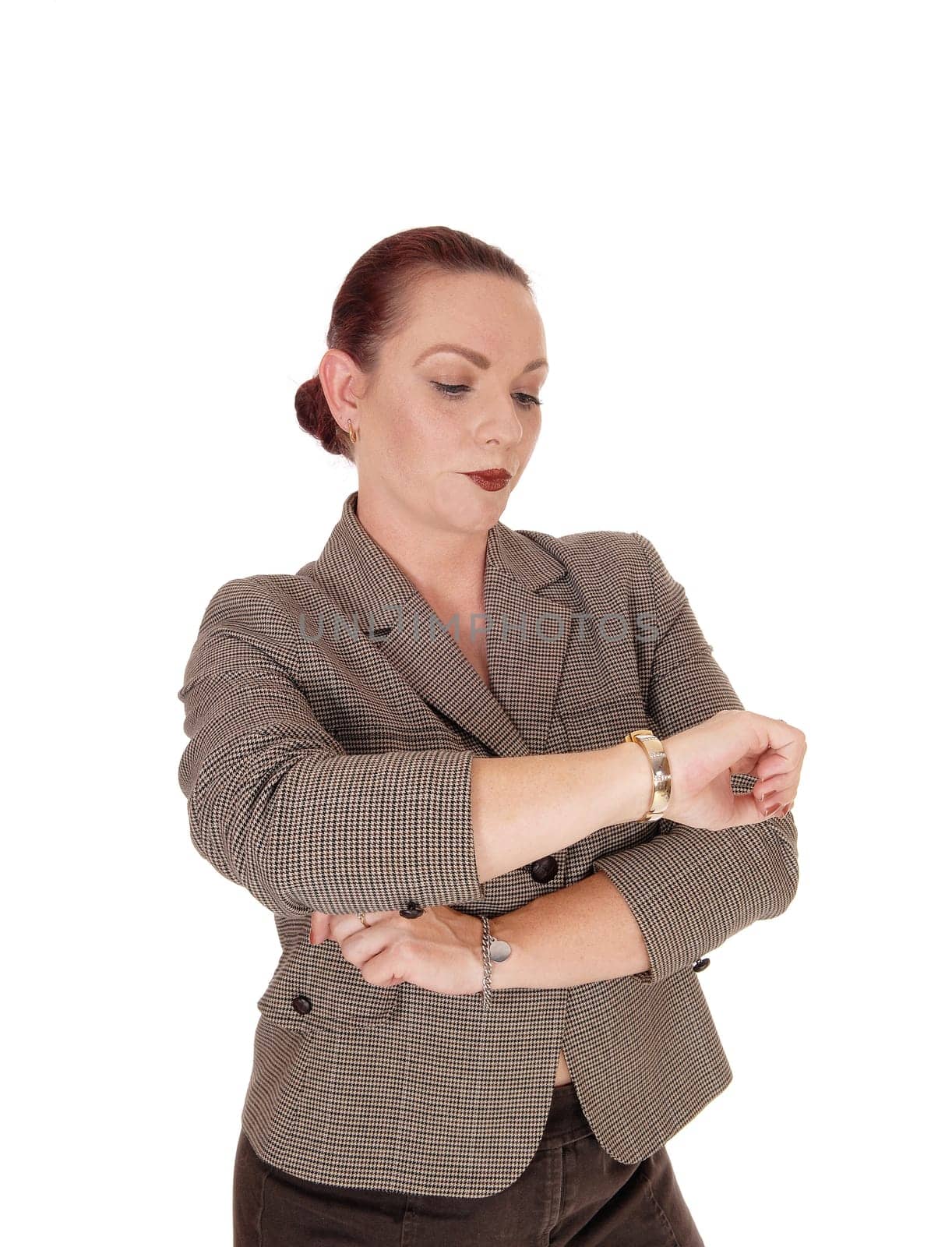 A serious looking woman in a brown jacket standing and looking at.her wrist watch, isolated for white background.