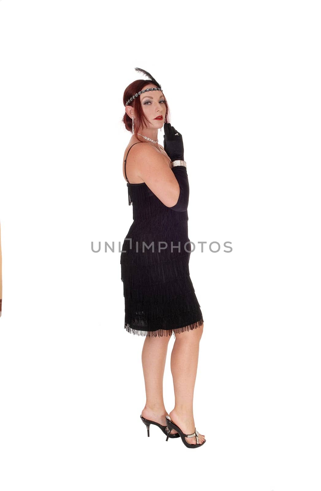 A beautiful woman standing in a black dress in profile with her .red hair and head band and cloves, isolated for white background.