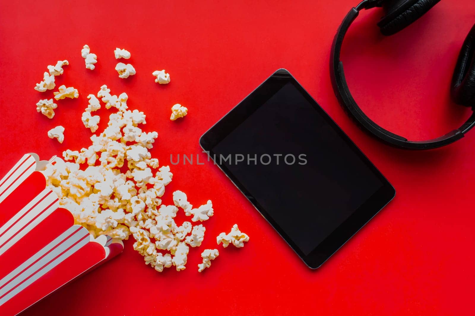 A tablet on a red background with popcorn and headphones