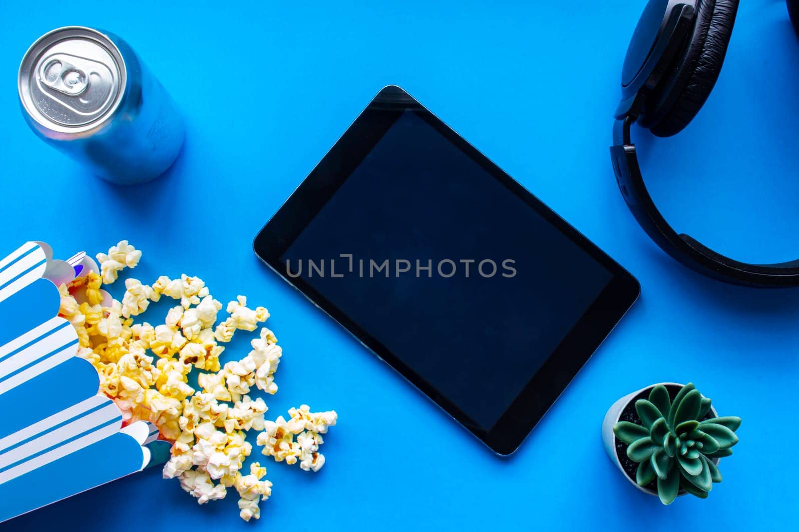 A tablet on a blue background with popcorn and headphones