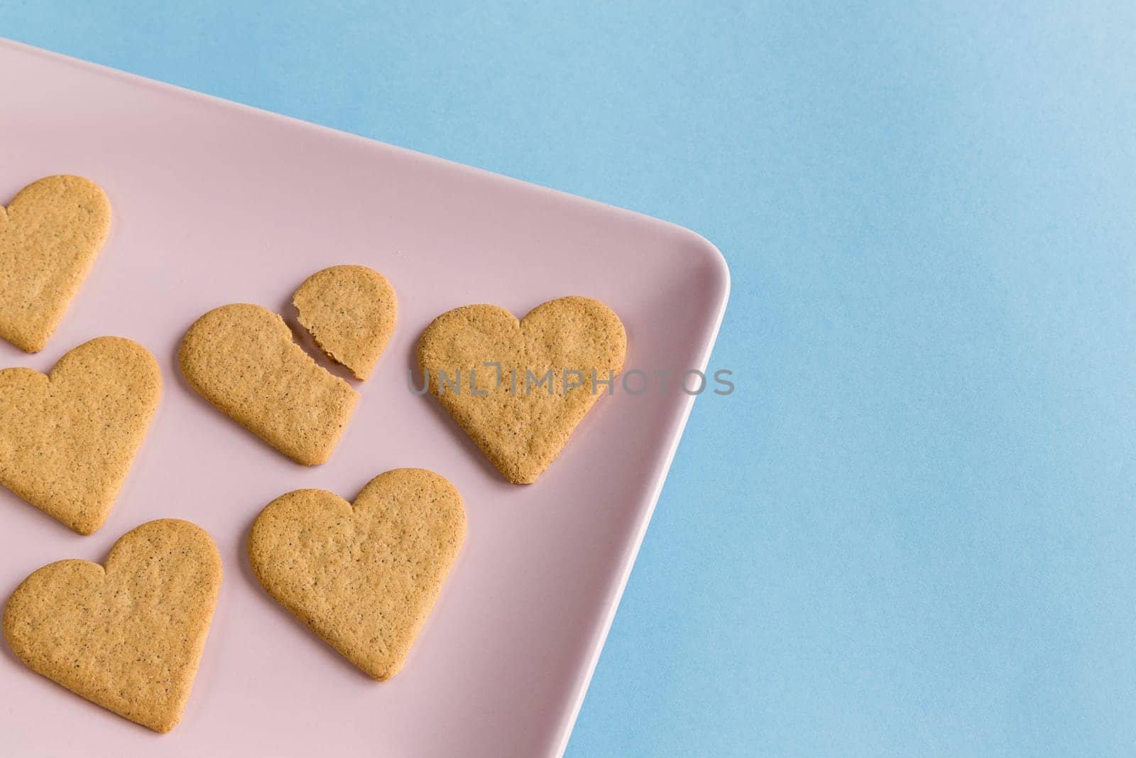Broken heart. Broken cookie in the middle of the complete ones on a pink tray and light blue background. Copy space.