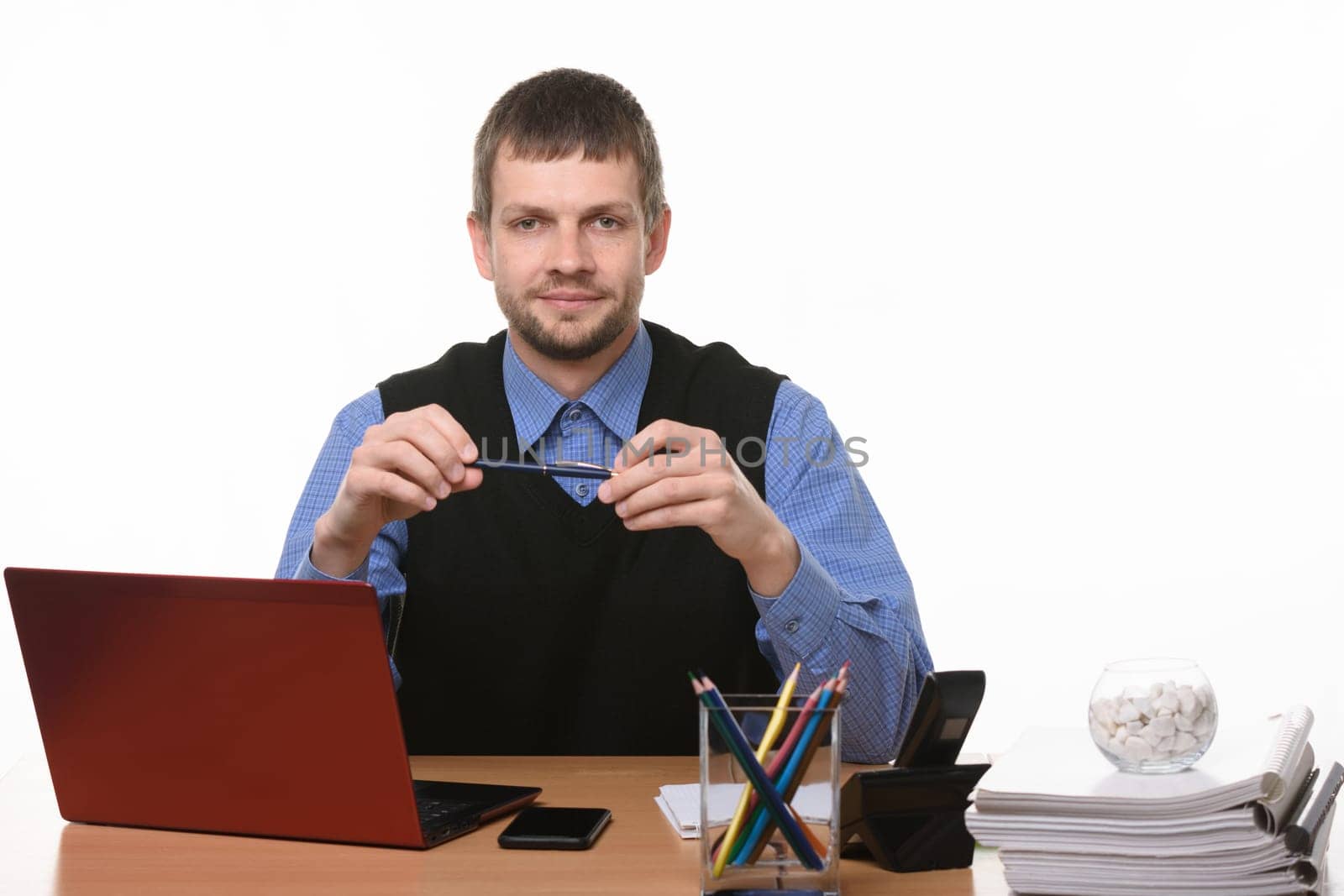 a man sits at an office table and holds a pen on a white background