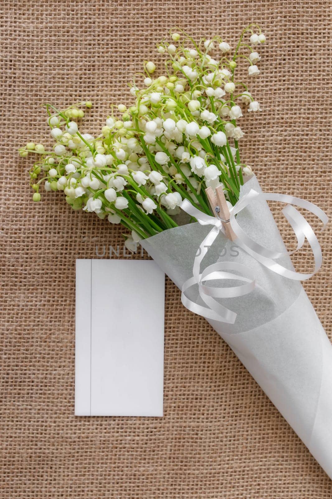 Lily of the valley flowers in a paper bag on blue background. Flat lay, top view, copy space
