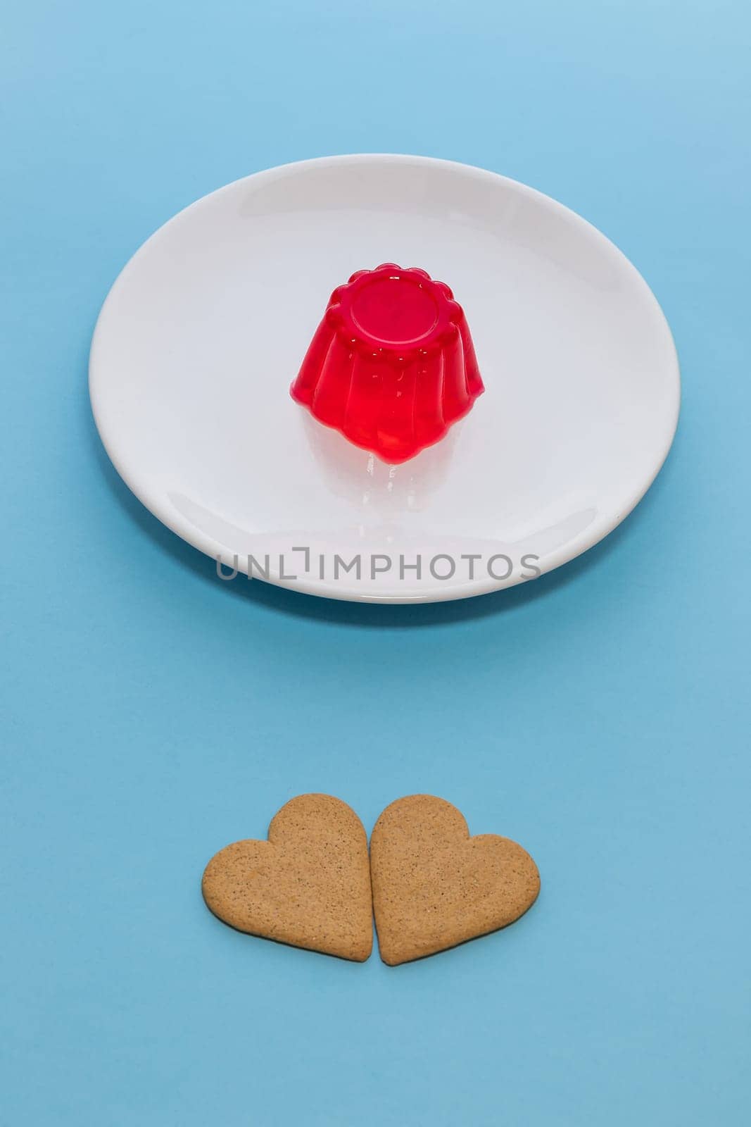 Close-up of a strawberry jelly dessert on a white plate. Two heart-shaped cookies.Light blue background