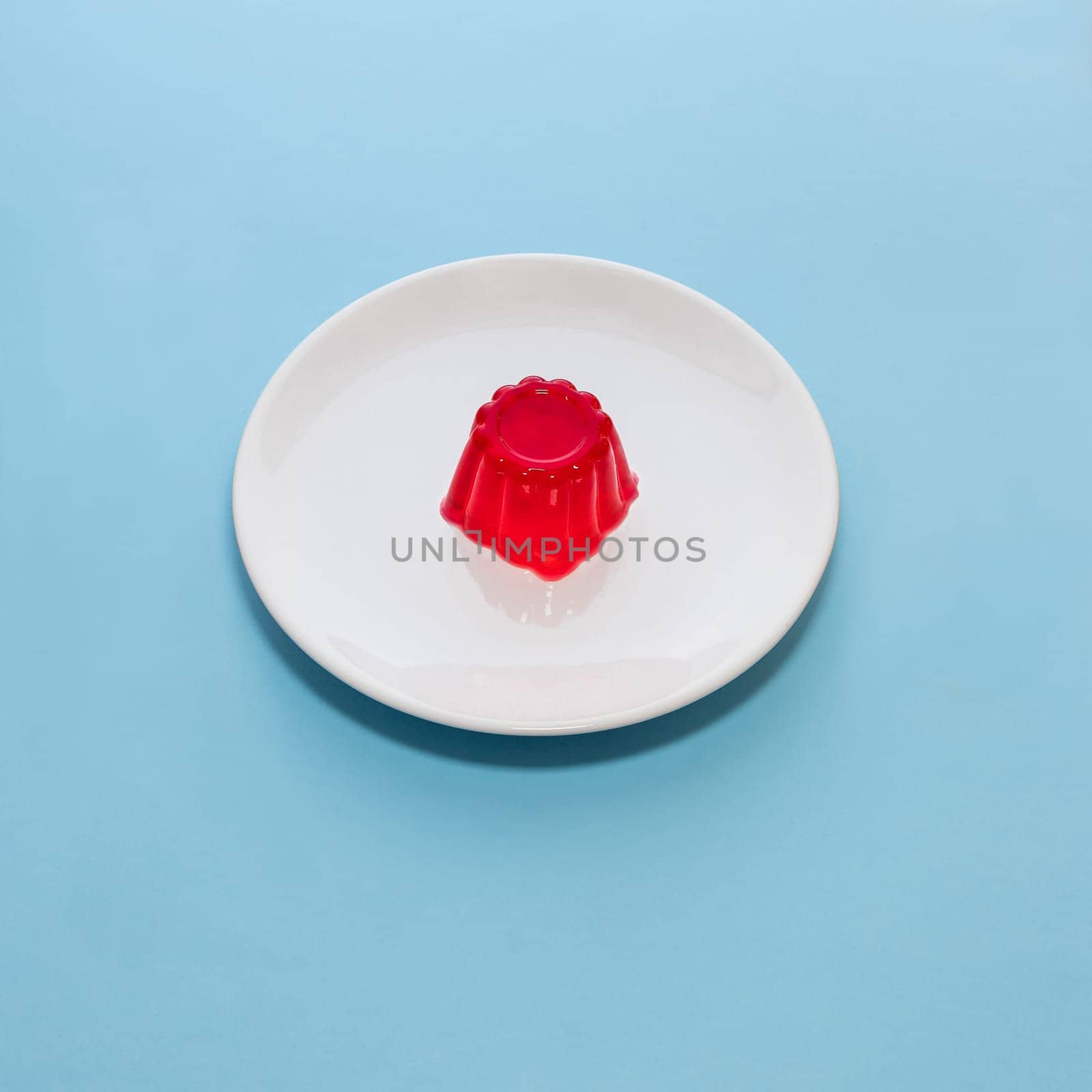 Close-up of a strawberry jelly dessert on a white plate with a light blue background