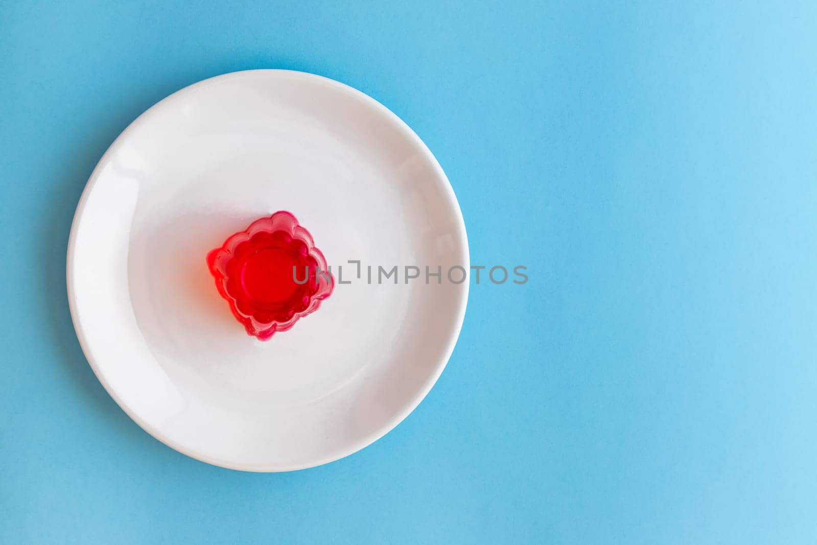 Close-up of a strawberry jelly dessert on a white plate with a light blue background. Copy space.