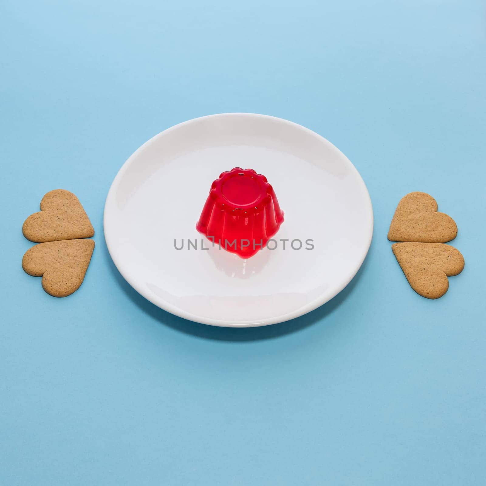 Close-up of a strawberry jelly dessert on a white plate. Heart-shaped cookies. Light blue background