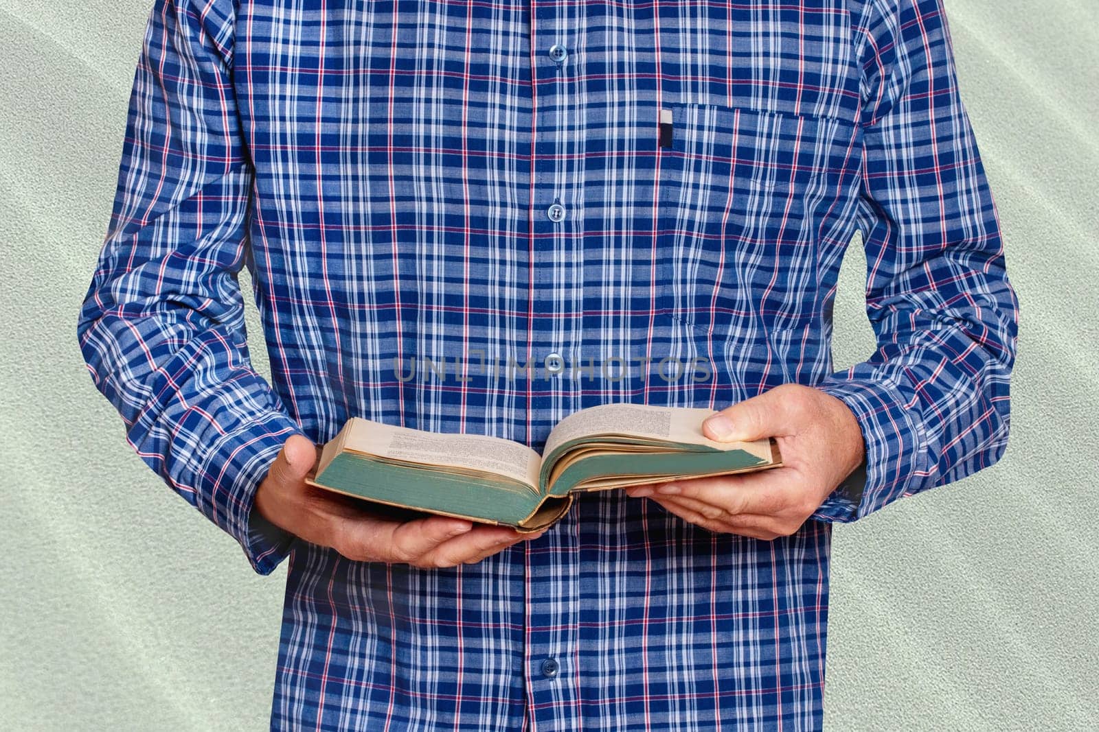 Closeup of hands from a man in a blue and white striped shirt holds an old book in his hands and reads. Businessman in front of bright stone wall. Macro.