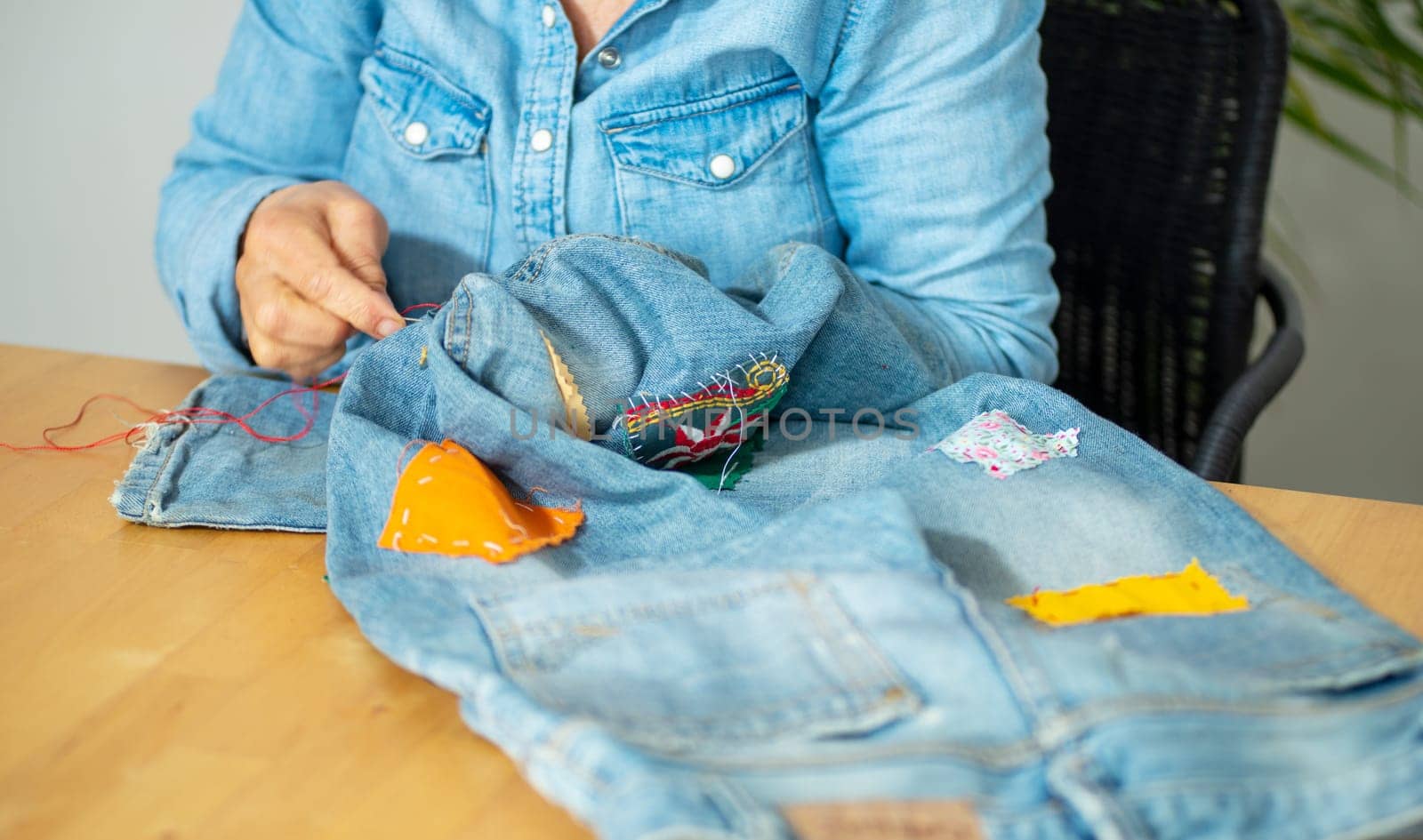 an elderly woman hands sewing on fabric jeans