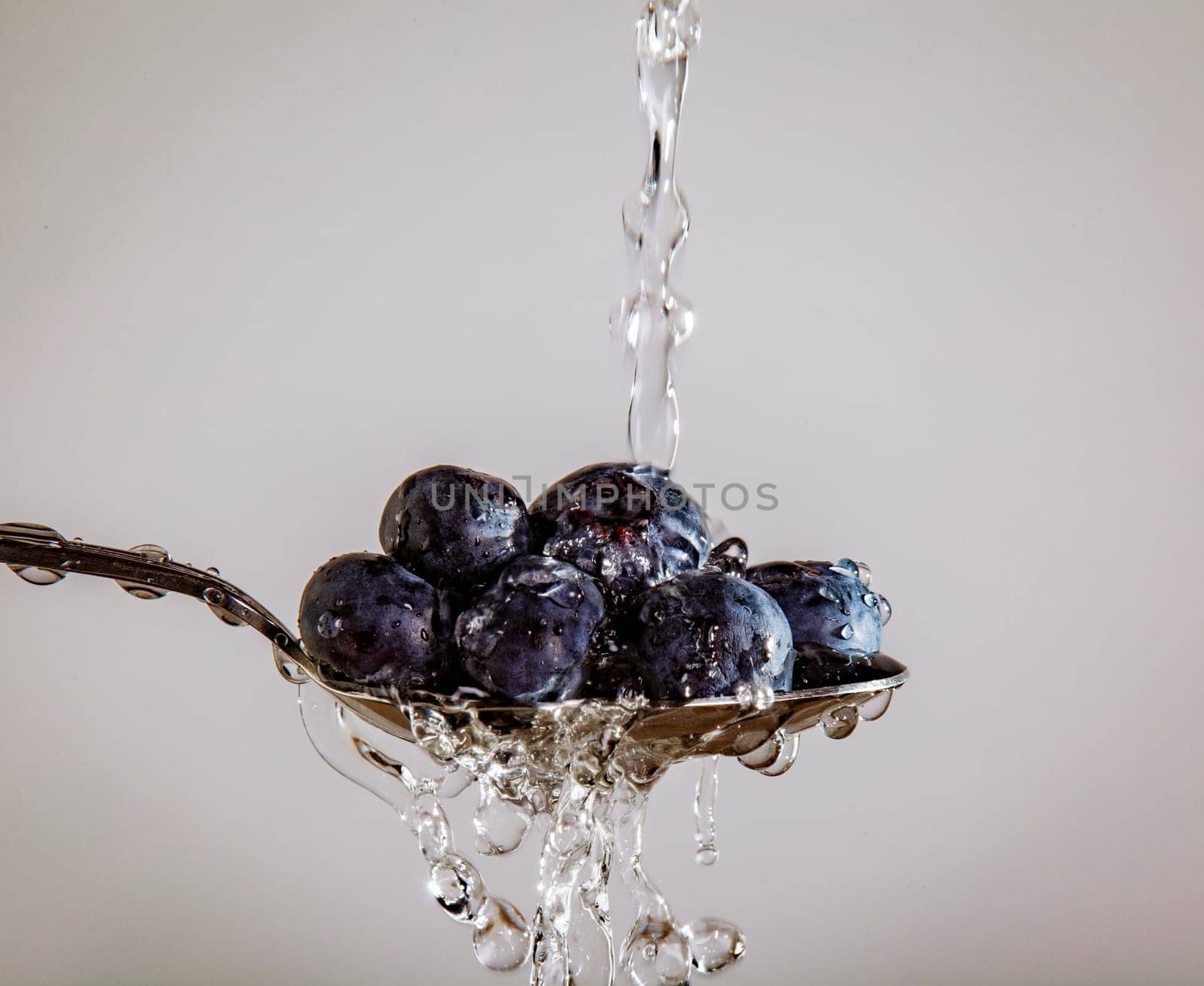 Blueberries on a Spoon being washed, on a white background