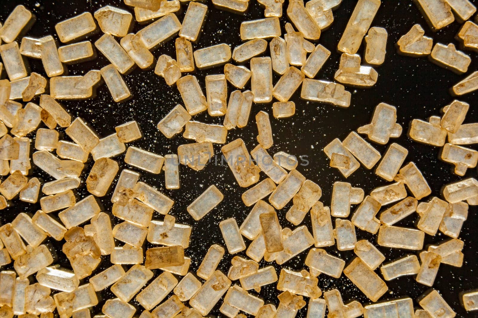 Macro of refined crystallised sugar with rectangular golden granules on a dark background