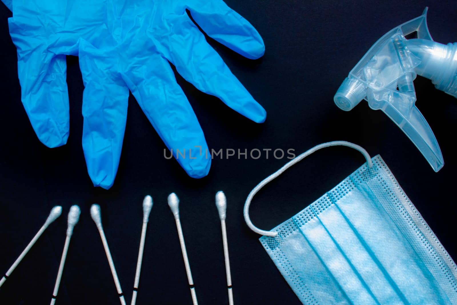 A close up of medical items: throat swabs, gloves, medical face mask and spray disinfecting liquid spray on a black background.