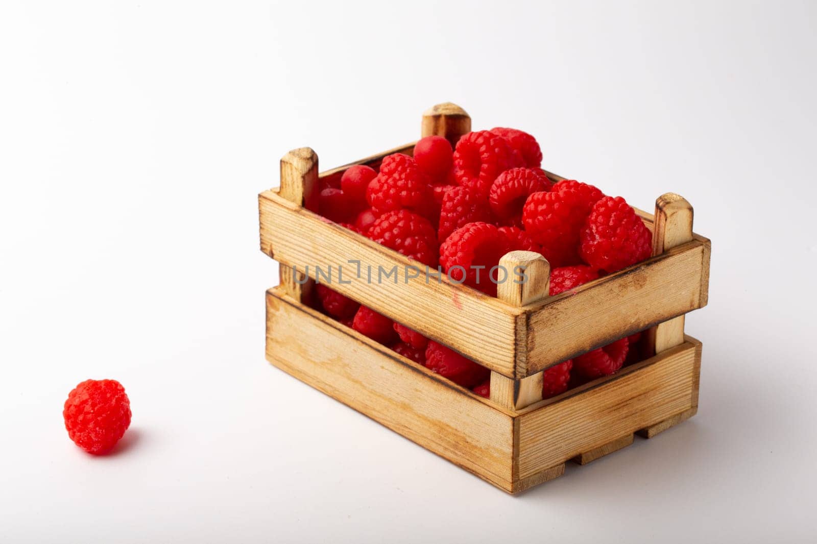 Some raspberries in a small wooden box on a white background