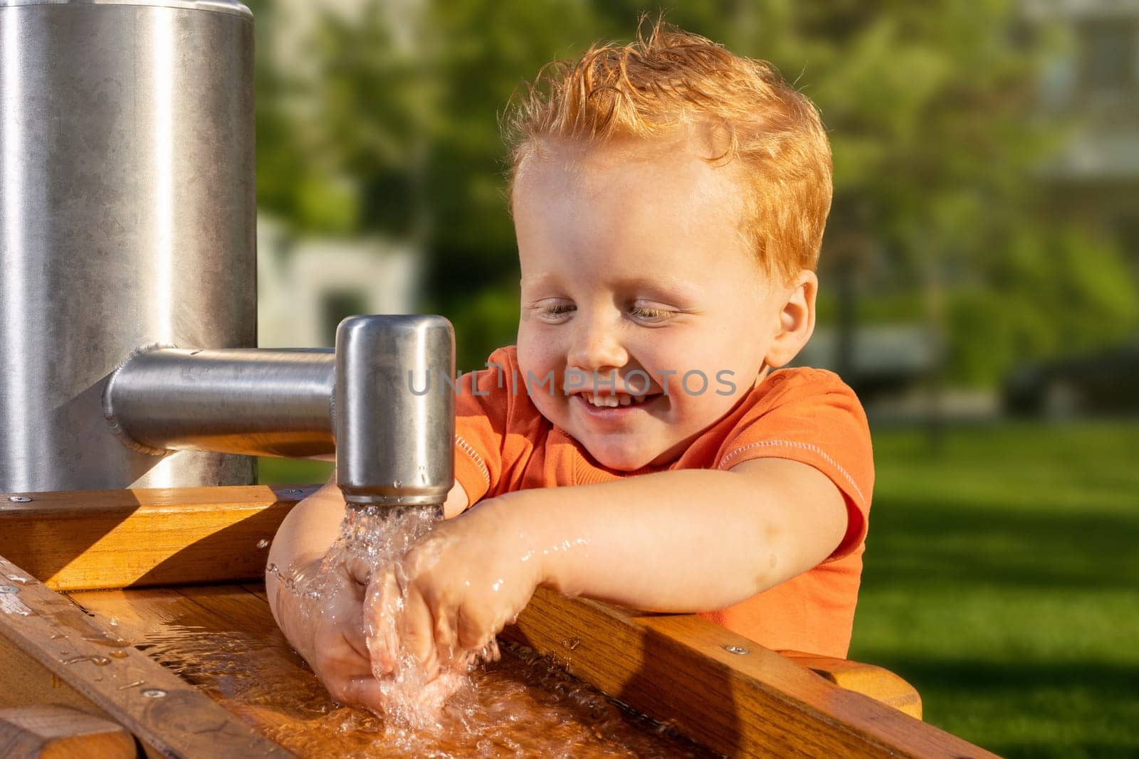 Smiling and happy little boy playing with tap water in a sunny playground
