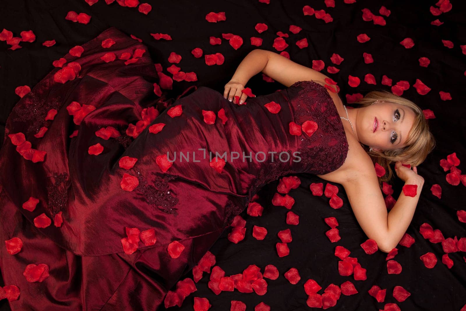 Attractive young woman in a red dress lying on back with flowers.