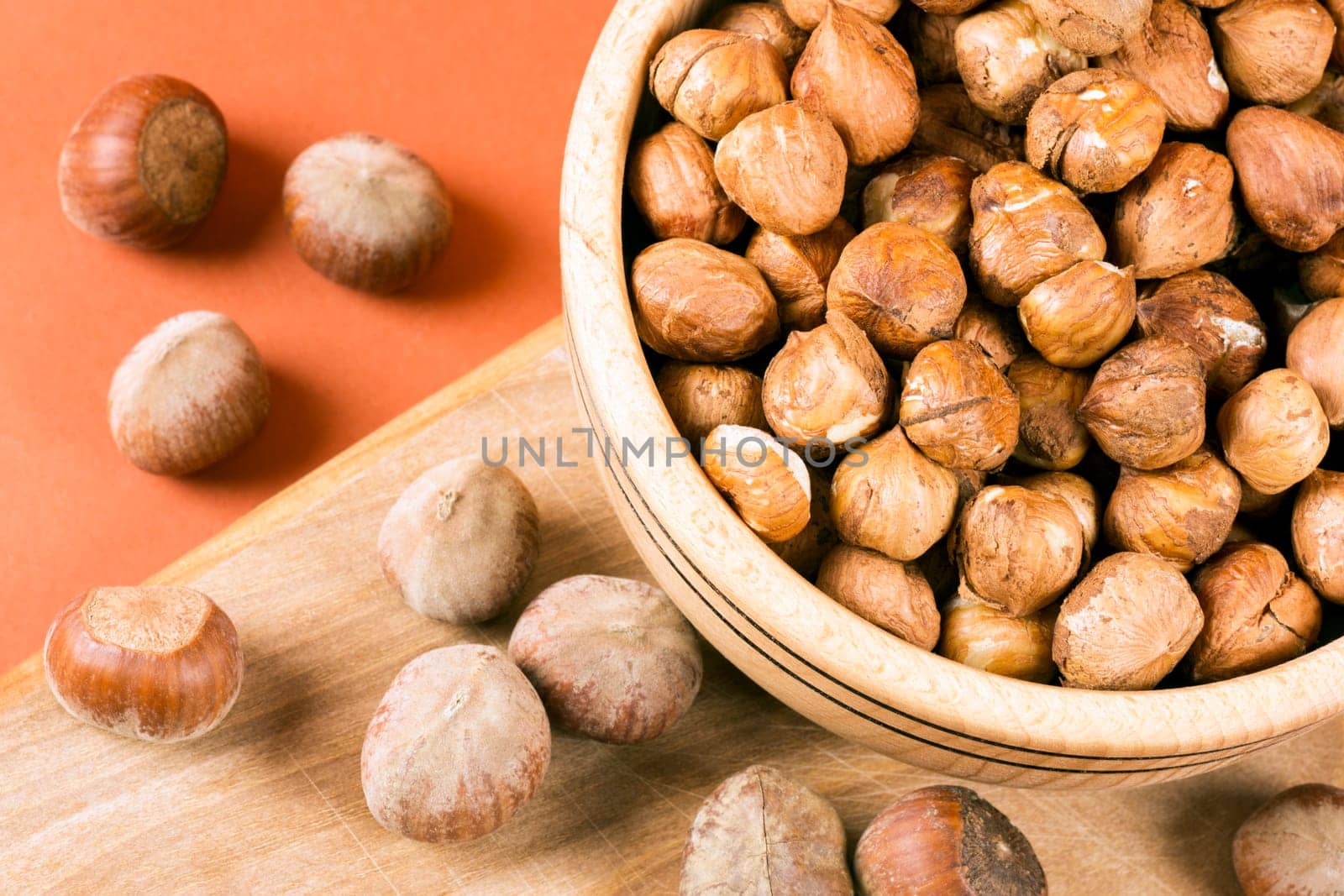 Close-up top view of whole hazelnut drupe fruit in wooden dish on cutting board.