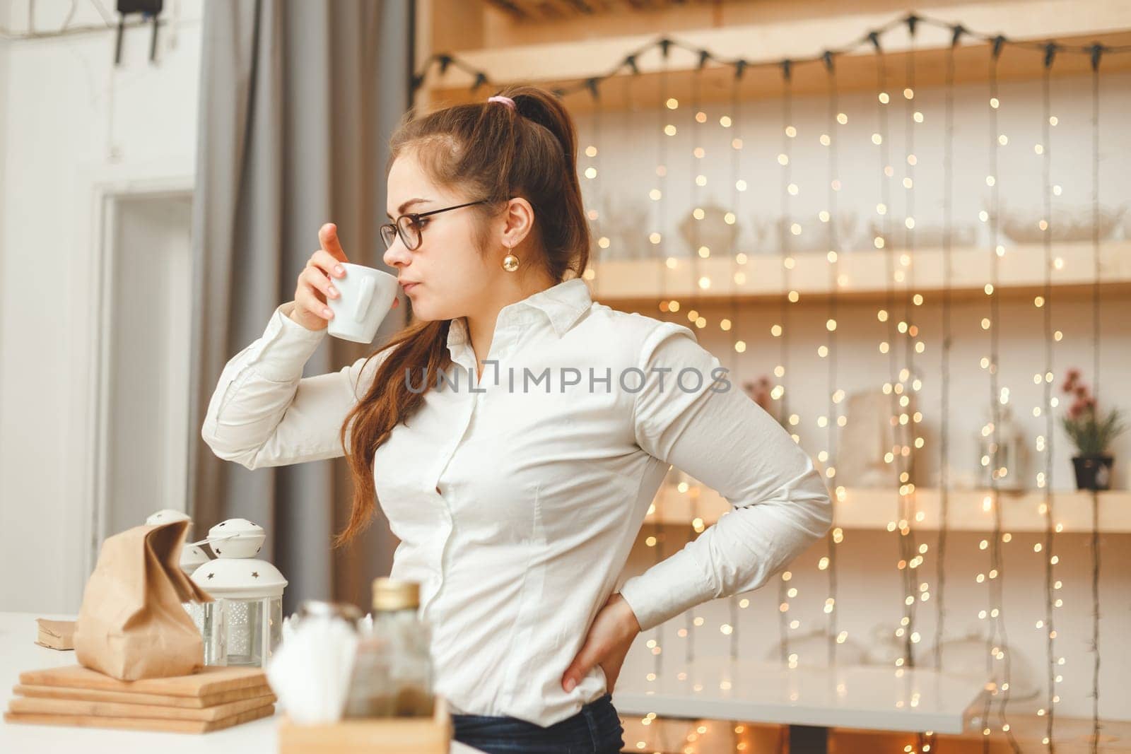 Young caucasian female entrepreneur drinking coffee and has a break. Side accidental view