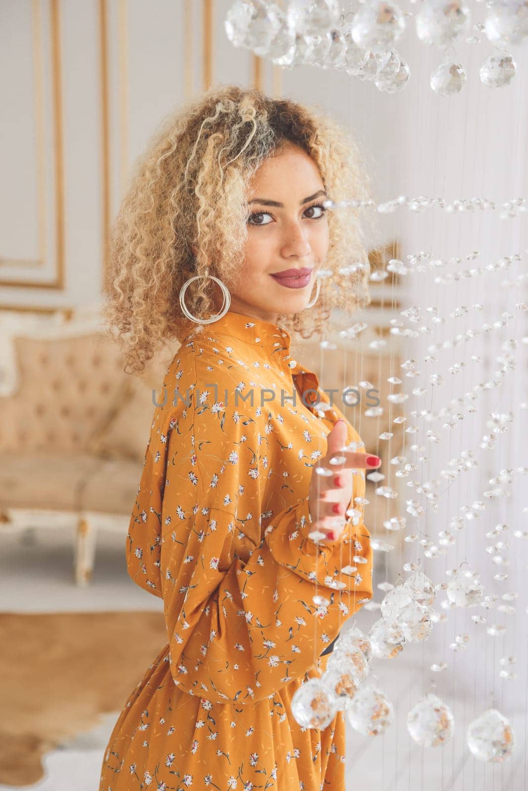 Luxury african mixed girl in fashionable dress posing near crystal chandelier in interior
