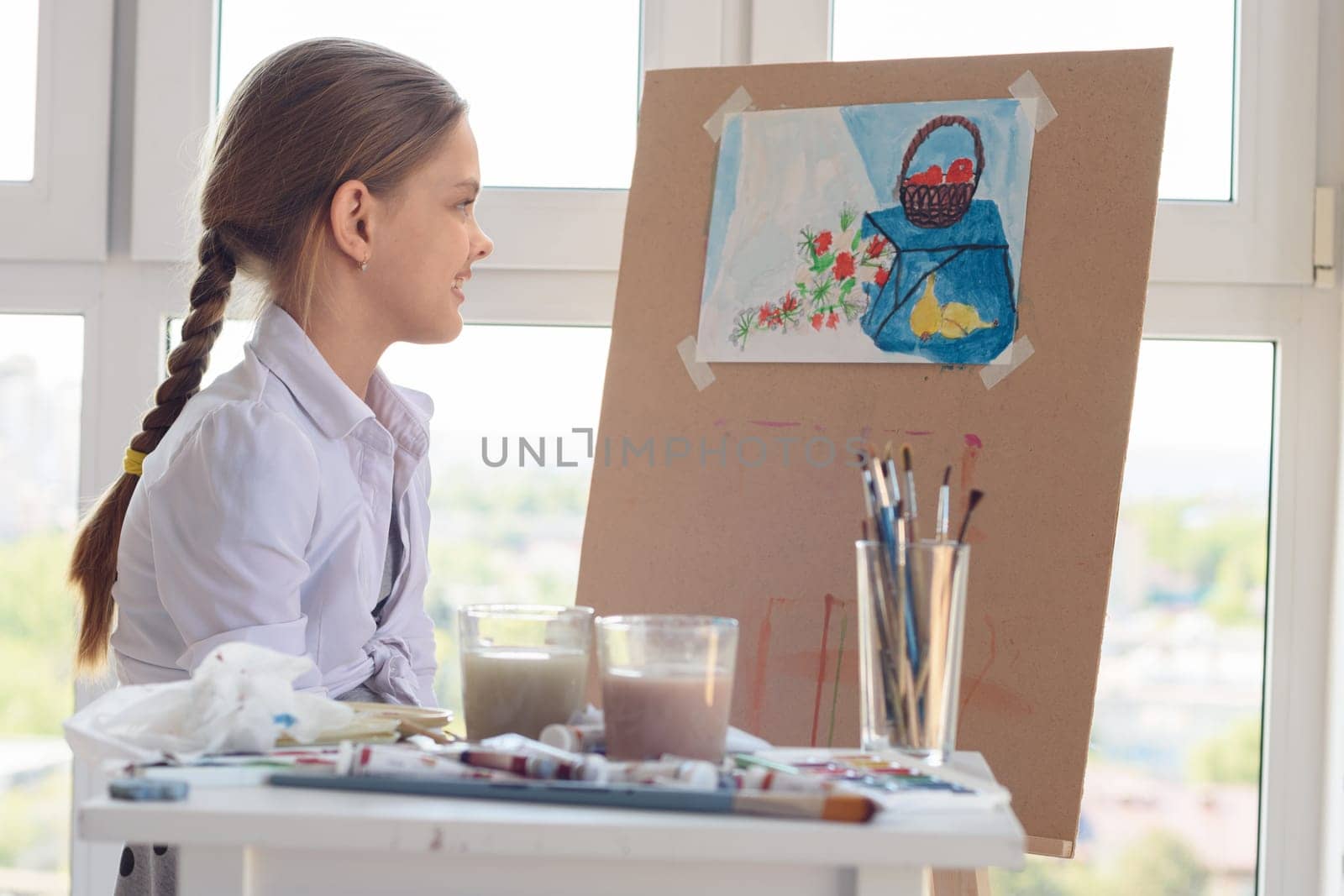 The girl happily looks at her finished drawing hanging on an easel