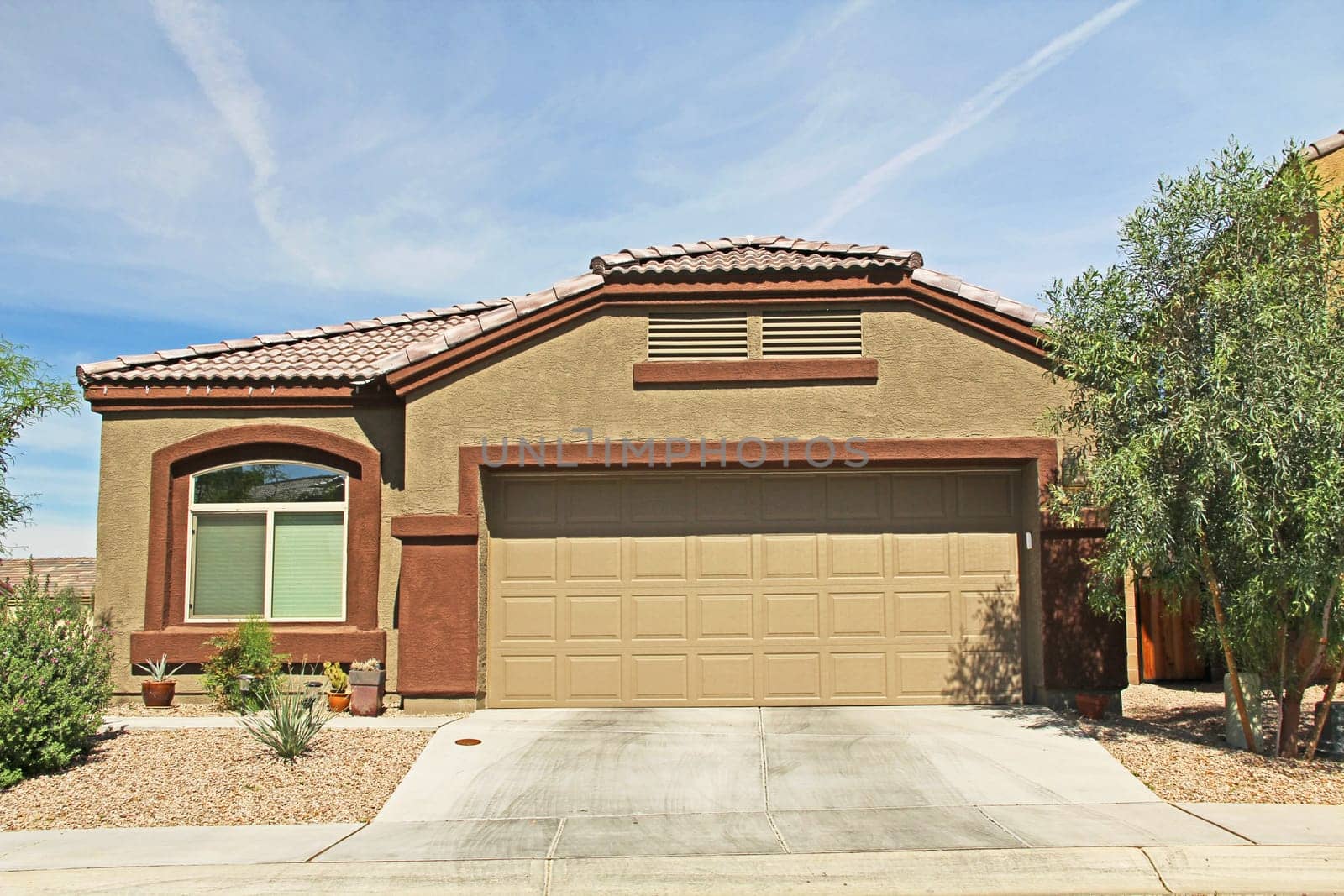 :  New one-story ranch tan and burnt orange stucco home in Tucson, Arizona, USA with beautiful blue sky and landscaping.