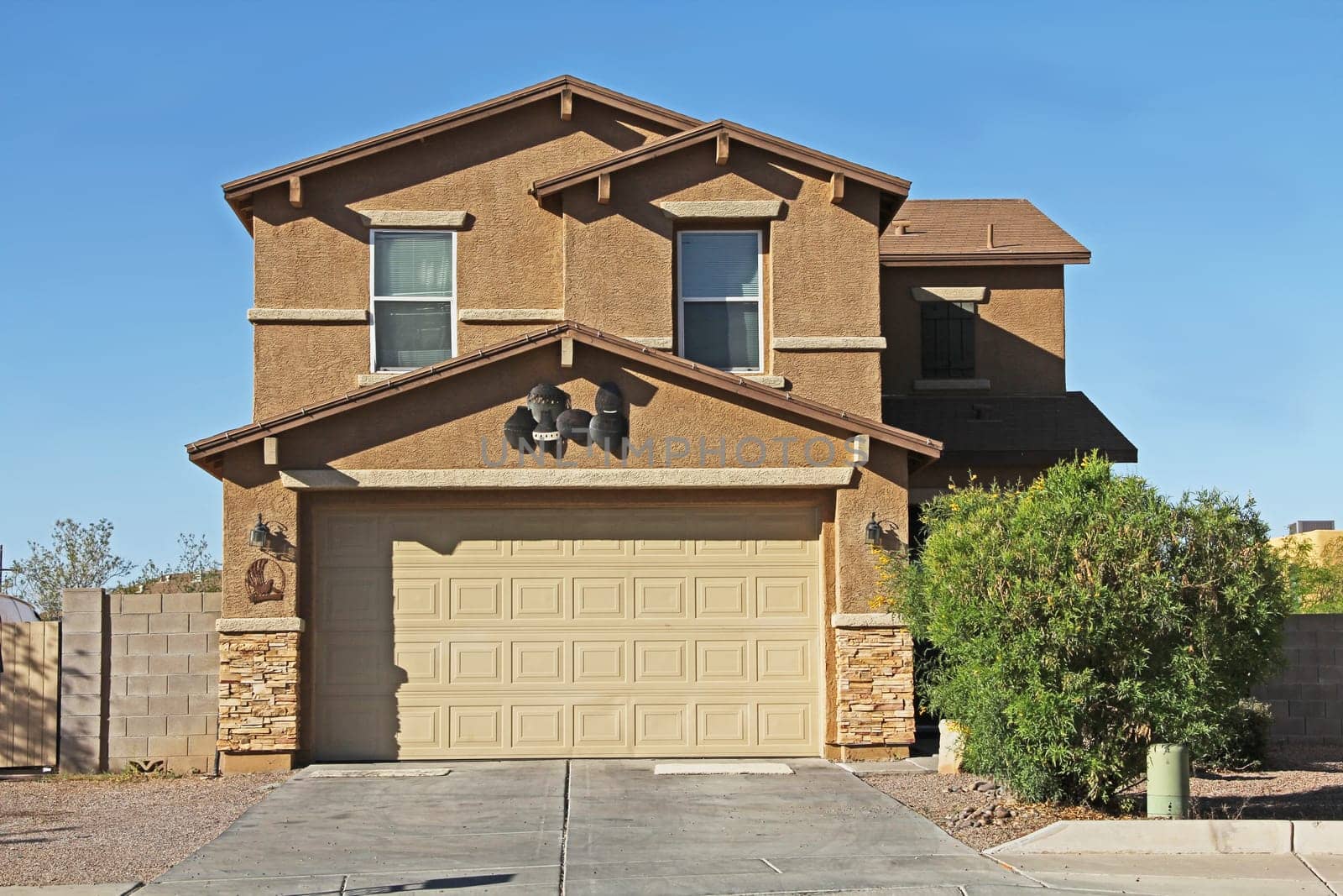 New two-story tan and brown stucco home in Tucson, Arizona, USA with beautiful blue sky and landscaping.
