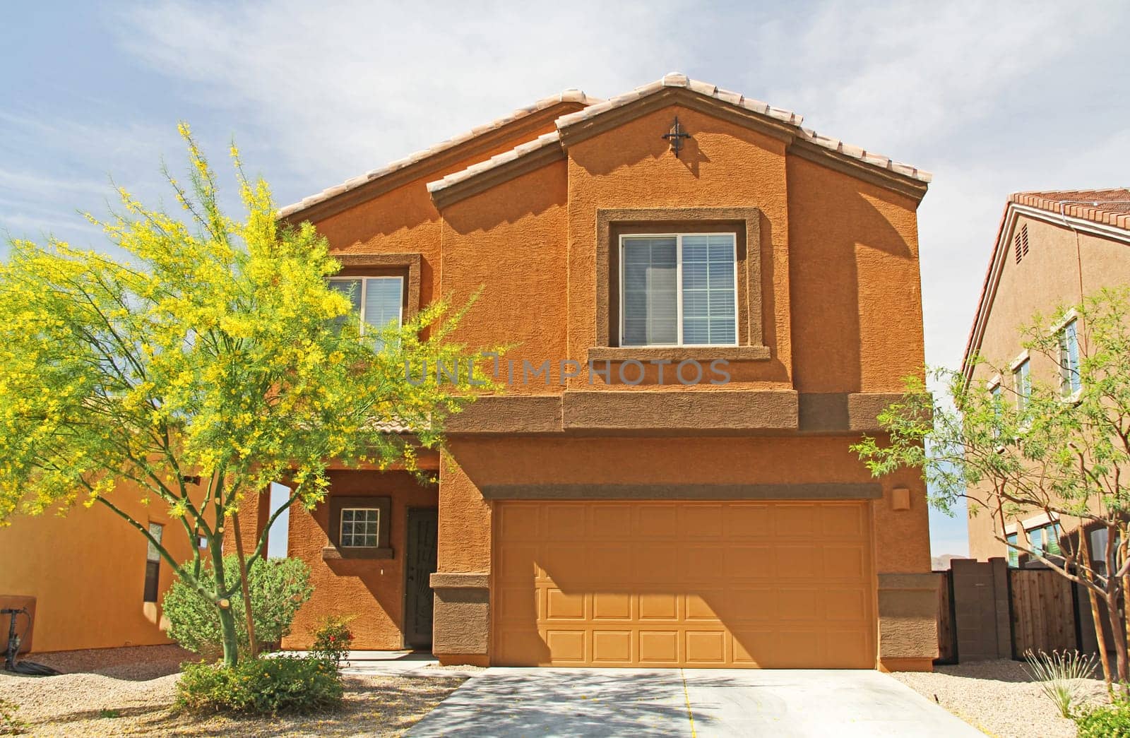 New two-story, brown and burnt orange stucco home in Tucson, Arizona, USA with beautiful blue sky and landscaping.