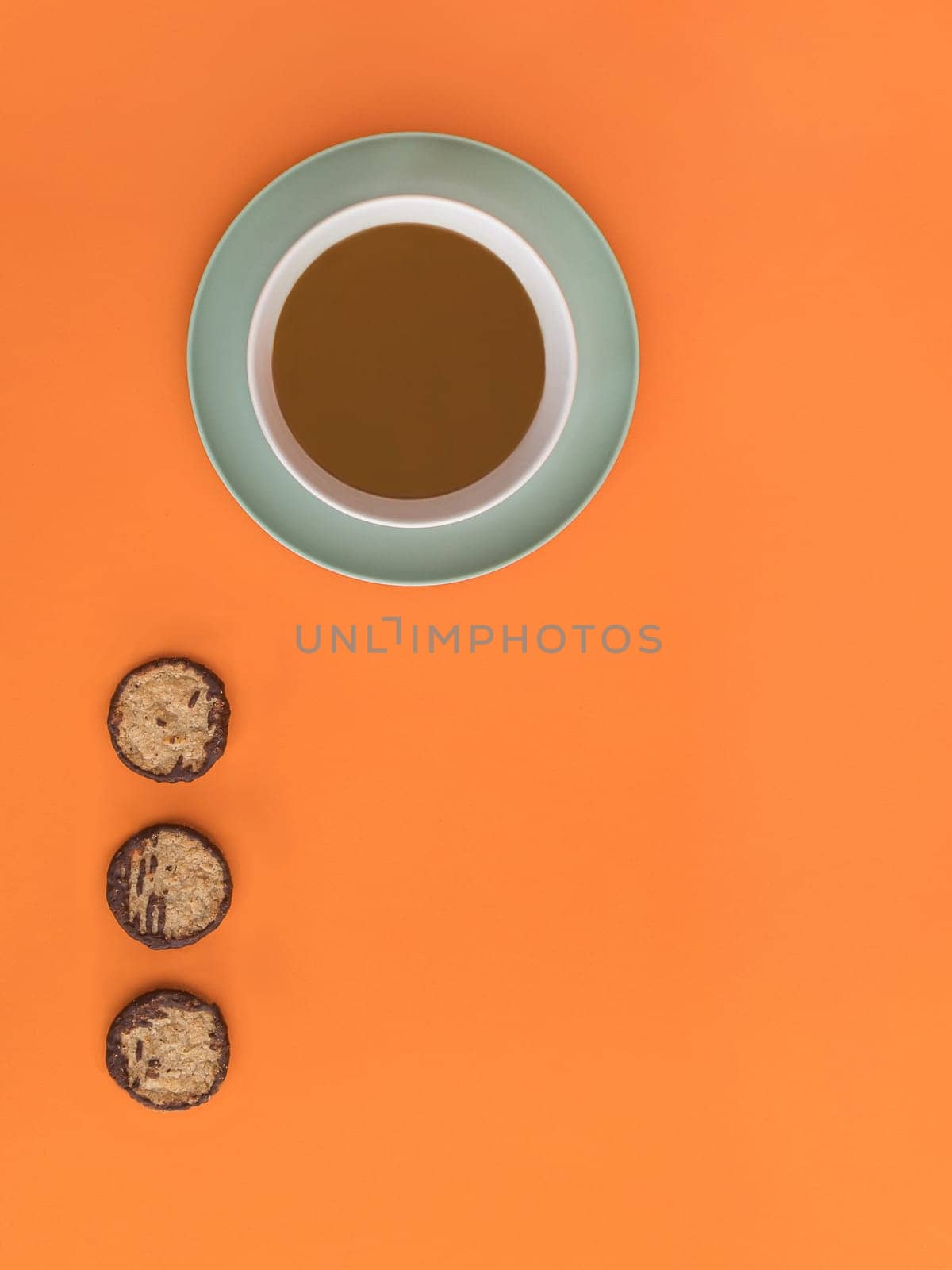 Chocolate bowl on a green light plate and three cookies. Orange background. Copy space.