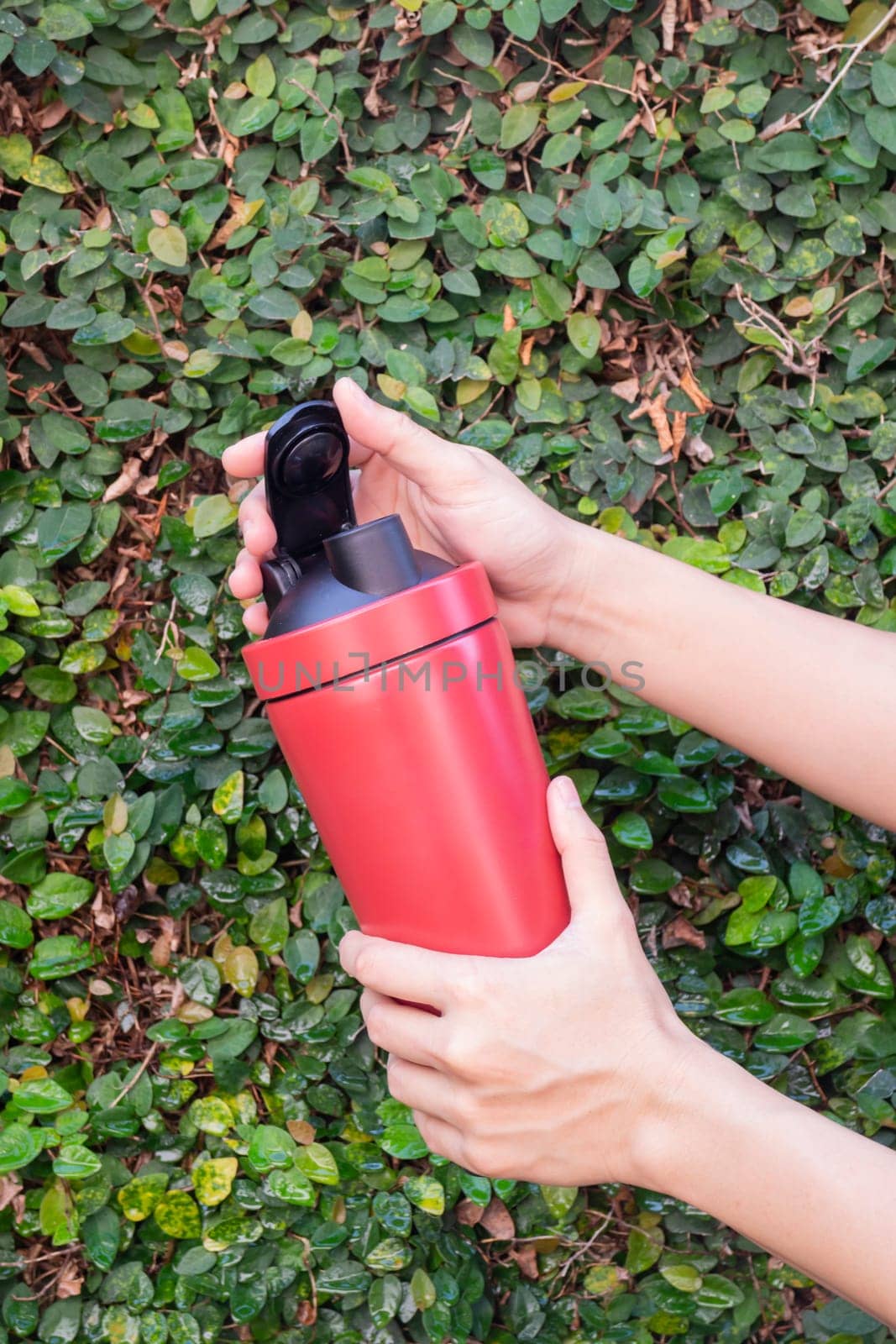 Aluminum thermos mug on hand with green leaves wall, stock photo