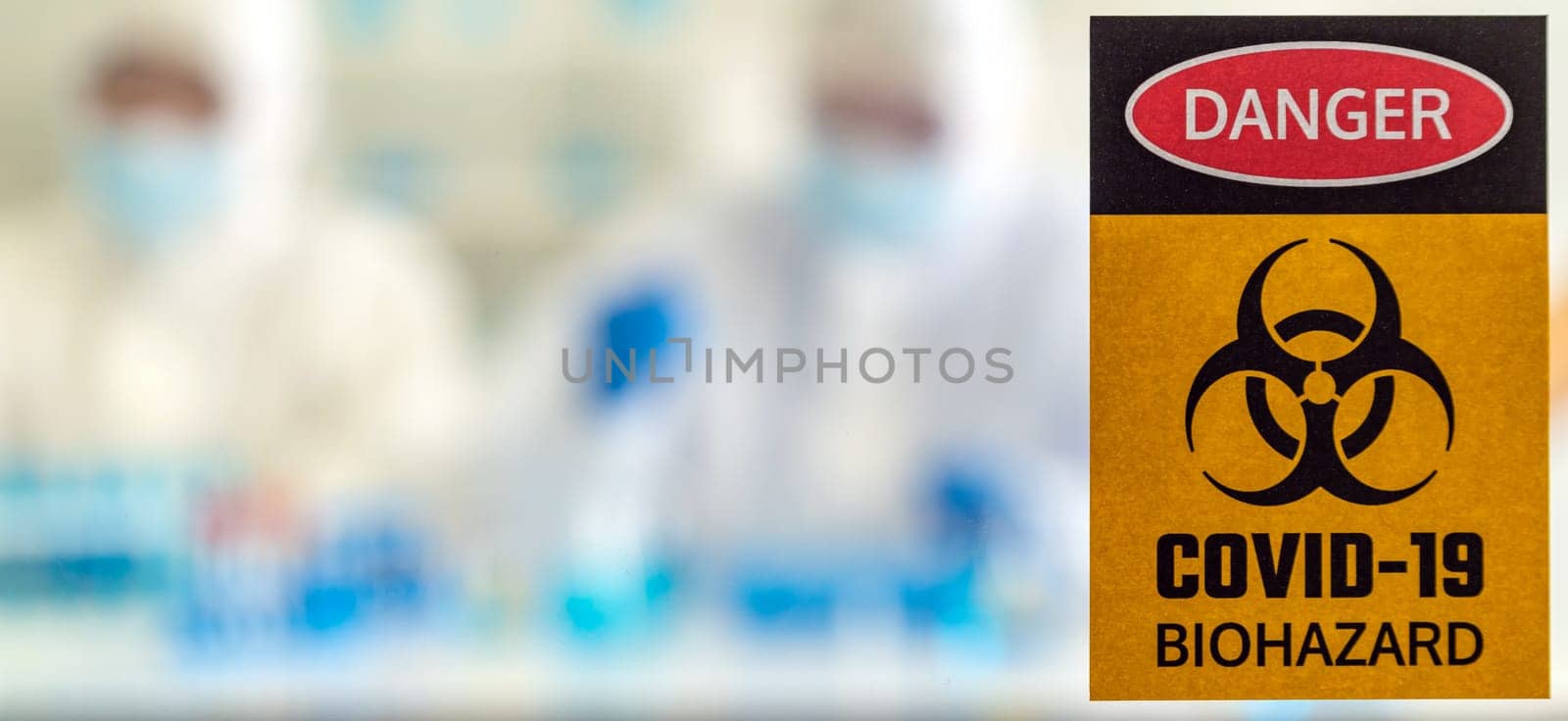 Panoramic Caution danger Signage of COVID-19 coronavirus in front of Laboratory room with background of Scientists working and researching vaccine for ncov-19 virus for world pandemic situation.