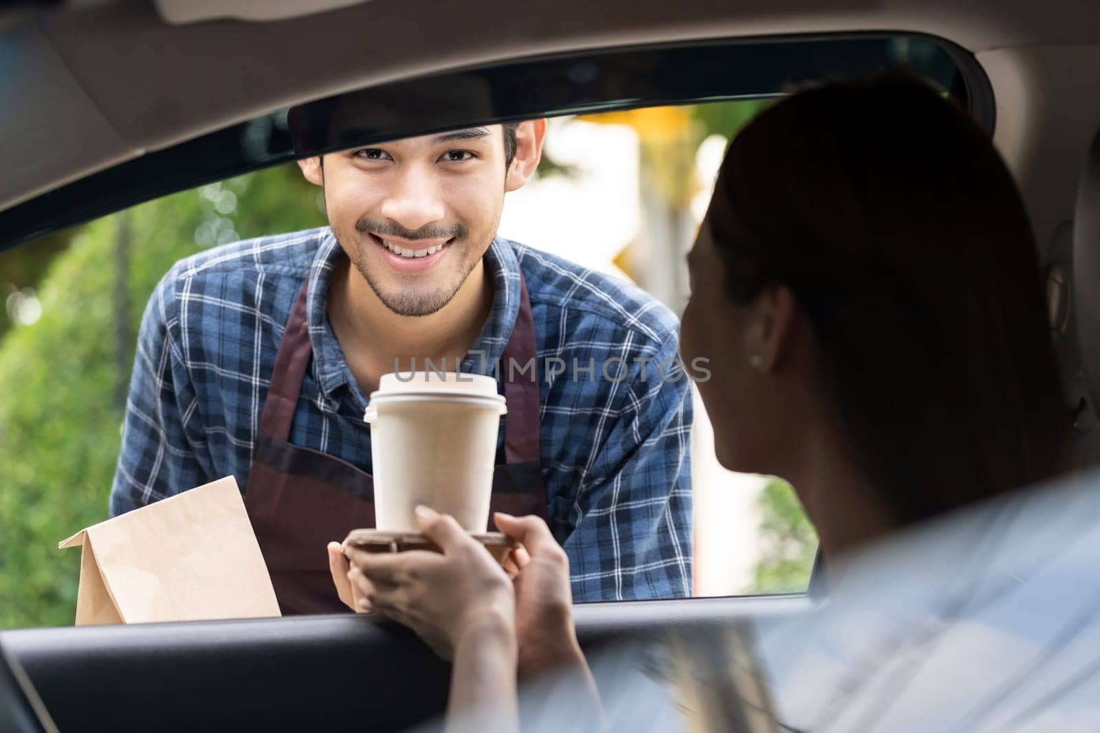 Waiter giving hot coffee cup with disposable tray and bakery bag through car window to customer at drive thru service station. Drive thru is popular service after coronavirus covid-19 pandemic.
