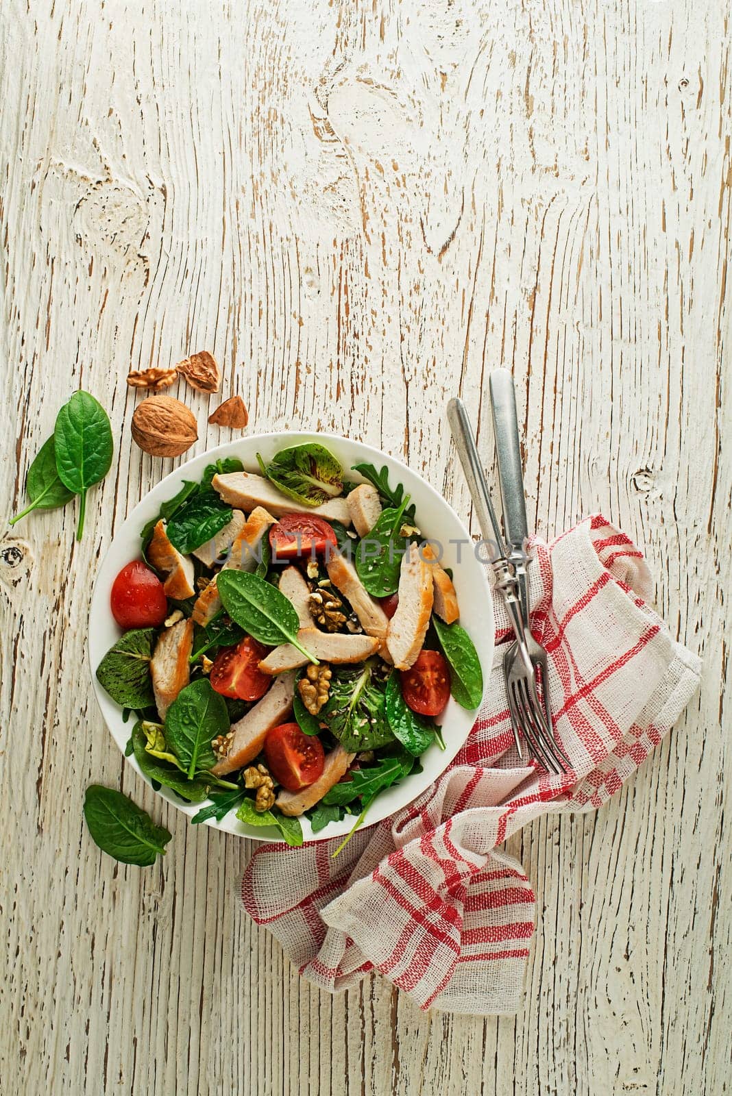 Healthy green salad with chicken breast, tomato and nuts on wooden table