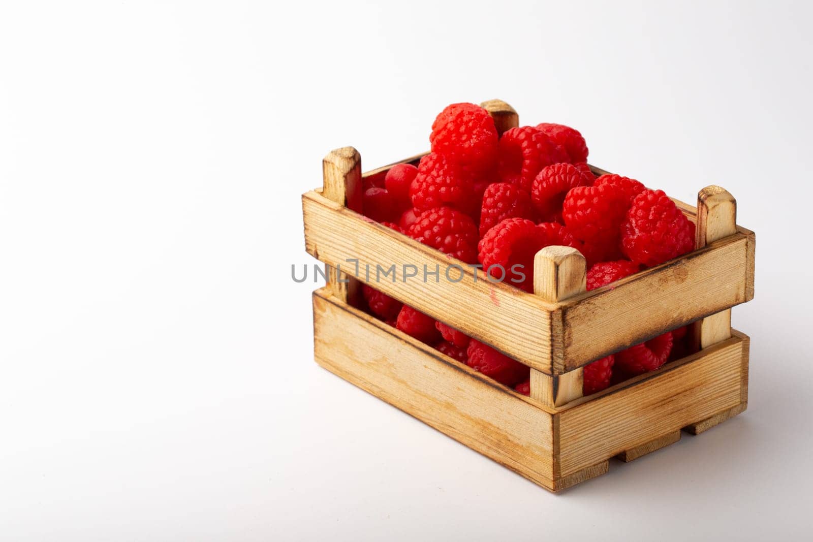 Some raspberries in a small wooden box on a white background