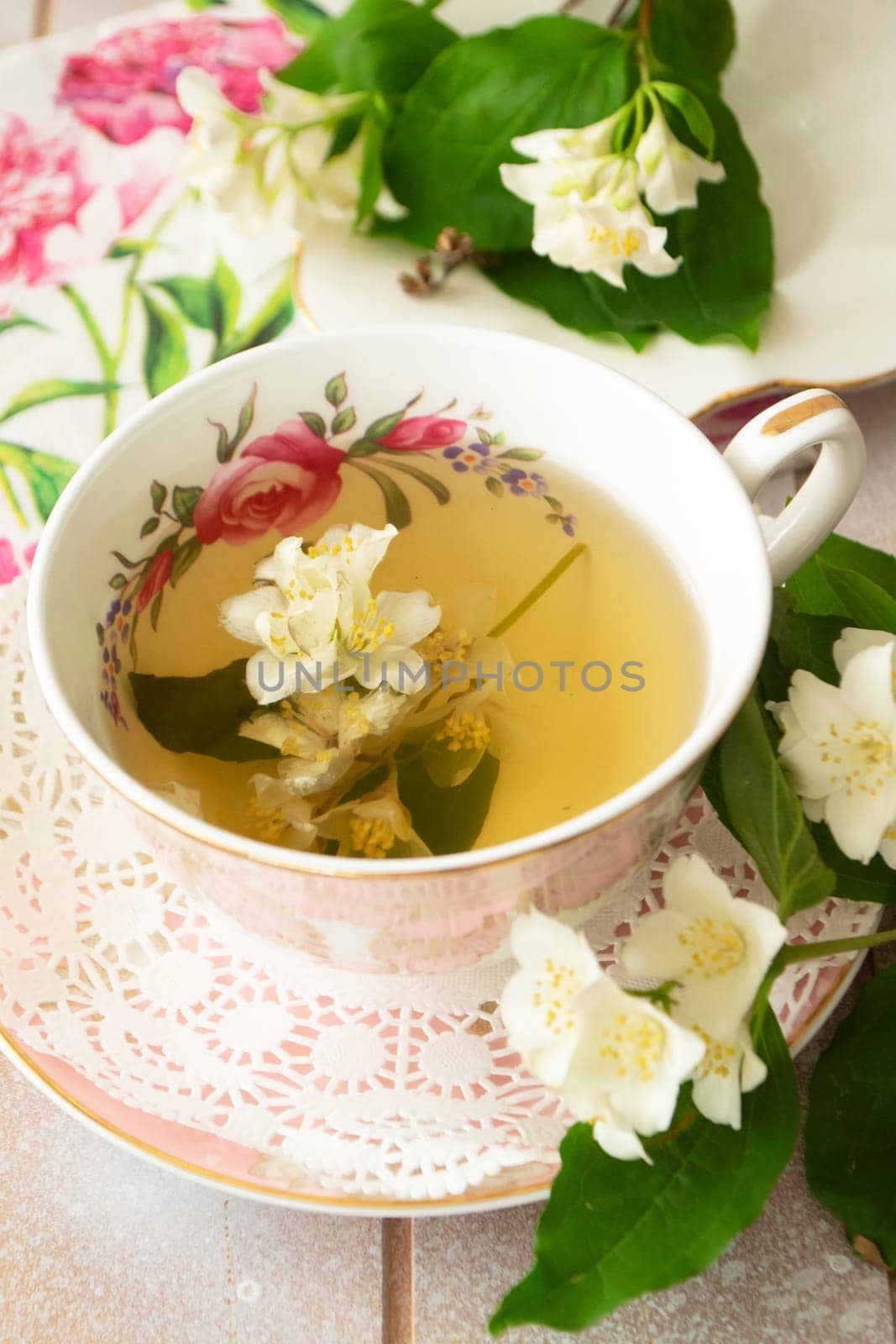 Vintage cup of hot green tea with jasmine flavor and fresh jasmine flowers. Vertical image