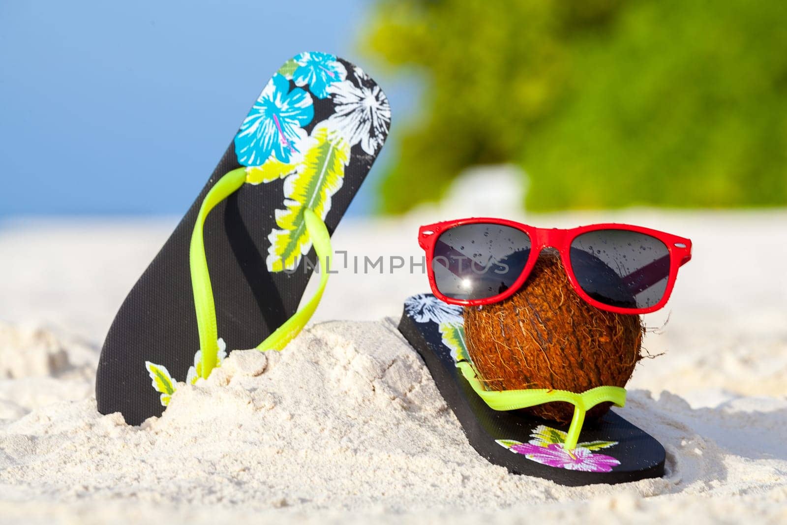 A coconut with sunglasses and shoes on the beach