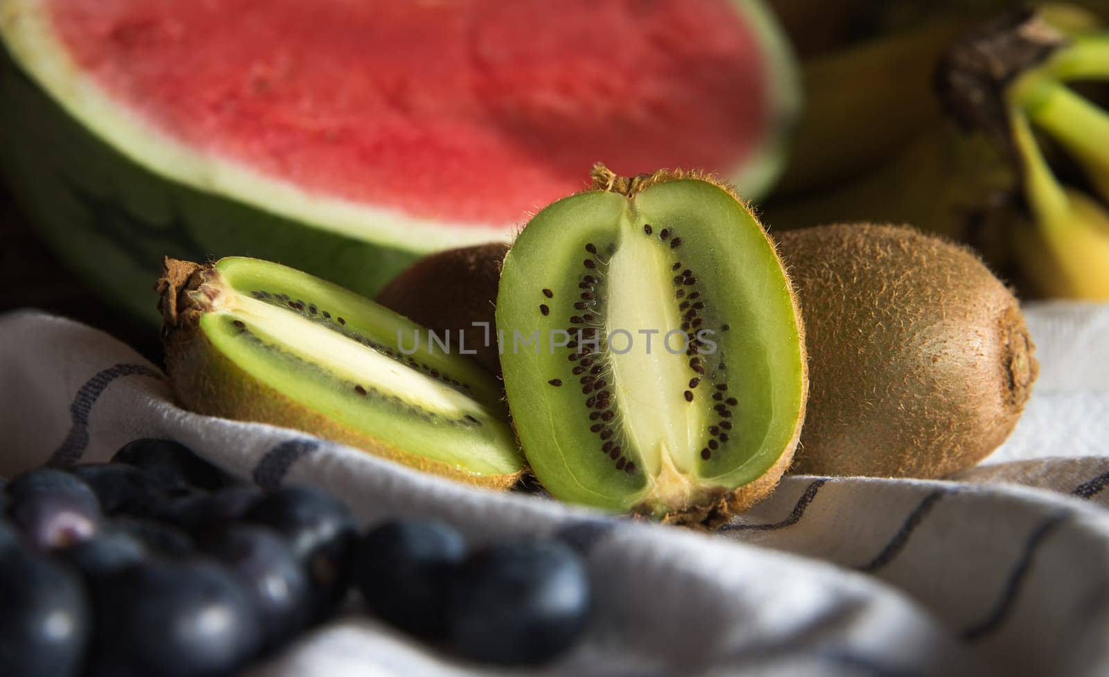 Fruits on a white tablecloth. Kiwis, watermelon, blueberries, bananas.