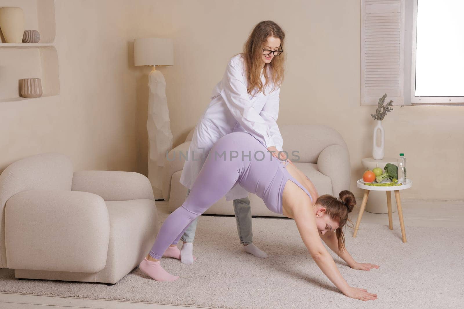 Fitness trainer helps overweight woman exercise at home, promoting flexibility, well-being and a healthy lifestyle in a cozy, modern interior.