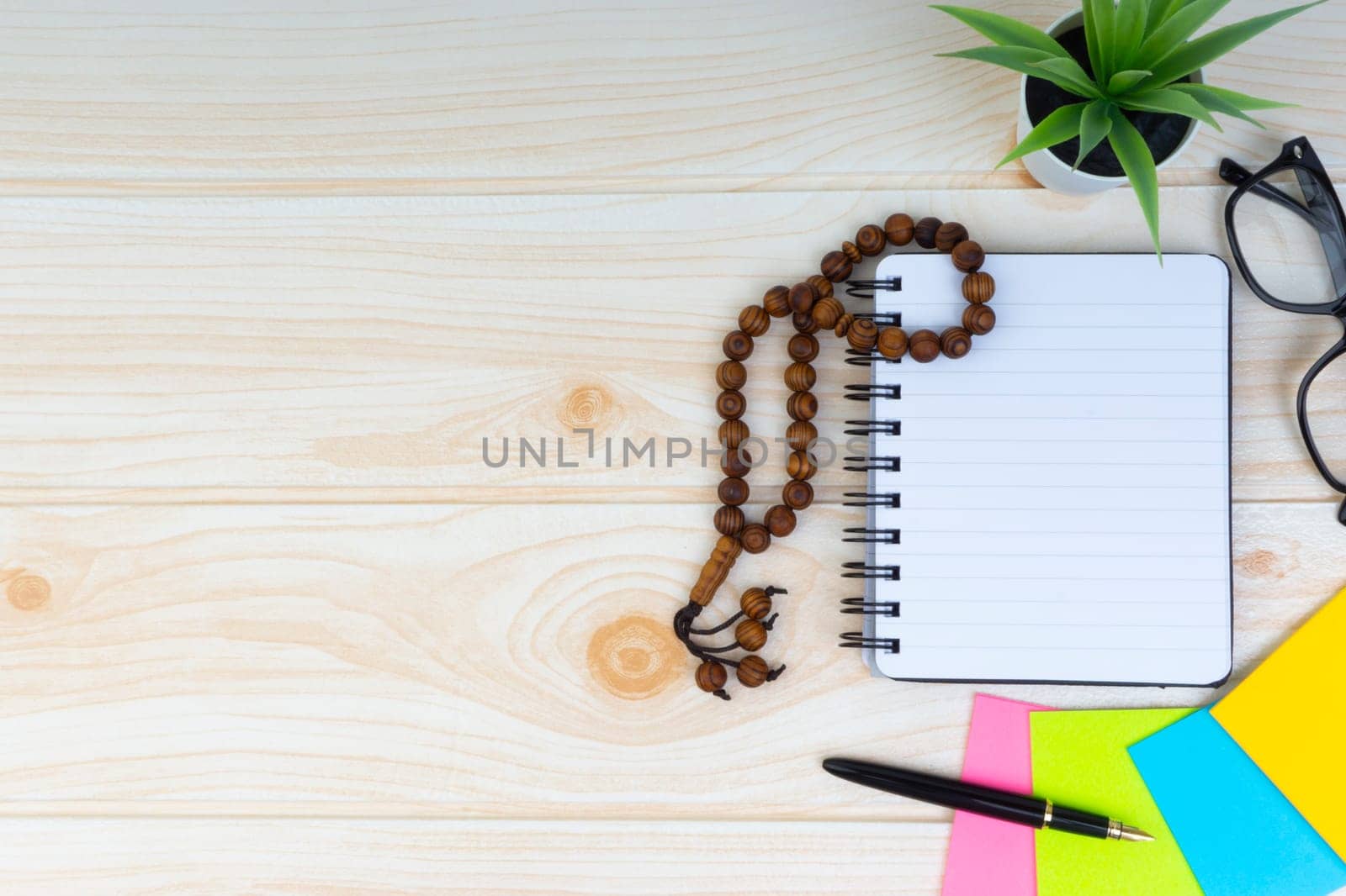 Flat lay view of workspace with Pen, spectacles, decoration flower, rosary and book.Copy Space, business and education concept.